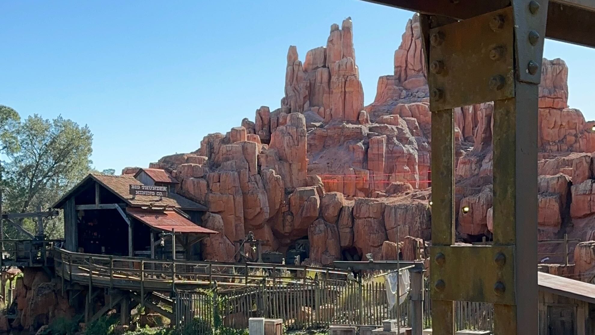 A wooden walkway and rustic building are set against a backdrop of red rock formations under a clear blue sky, offering the perfect setting for a daily recap amidst nature's beauty.