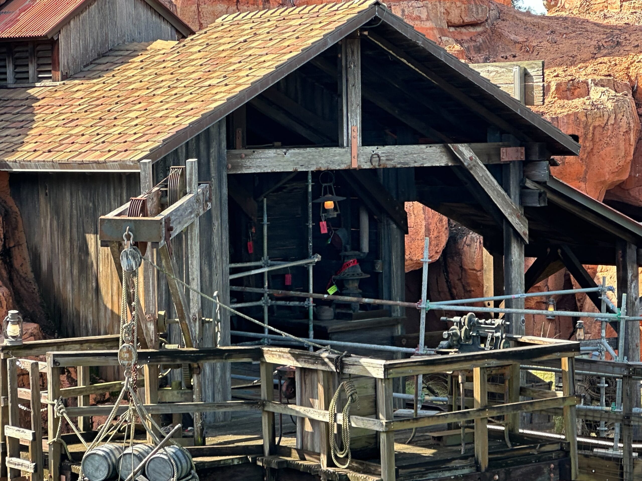 Rustic wooden structure with a sloped roof, featuring a pulley system and metal buckets. Surrounded by rocky terrain, giving a deserted, old-fashioned ambiance.