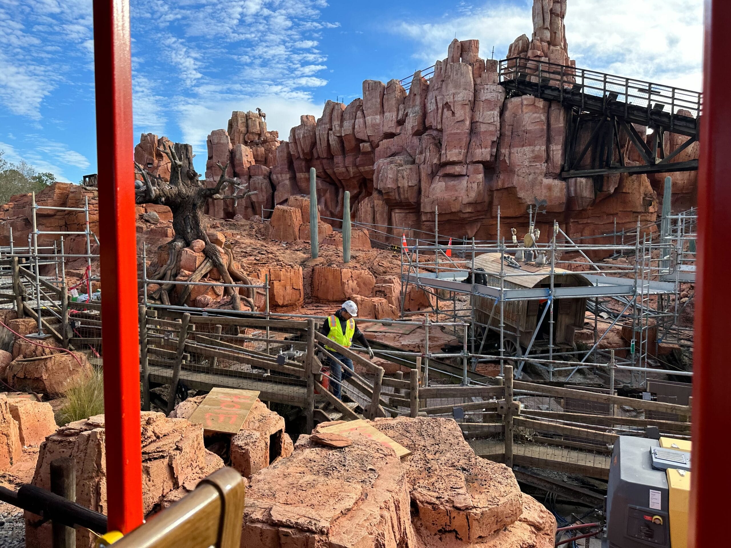 Construction workers on a site with scaffolding and reddish rock formations, set under a blue sky.