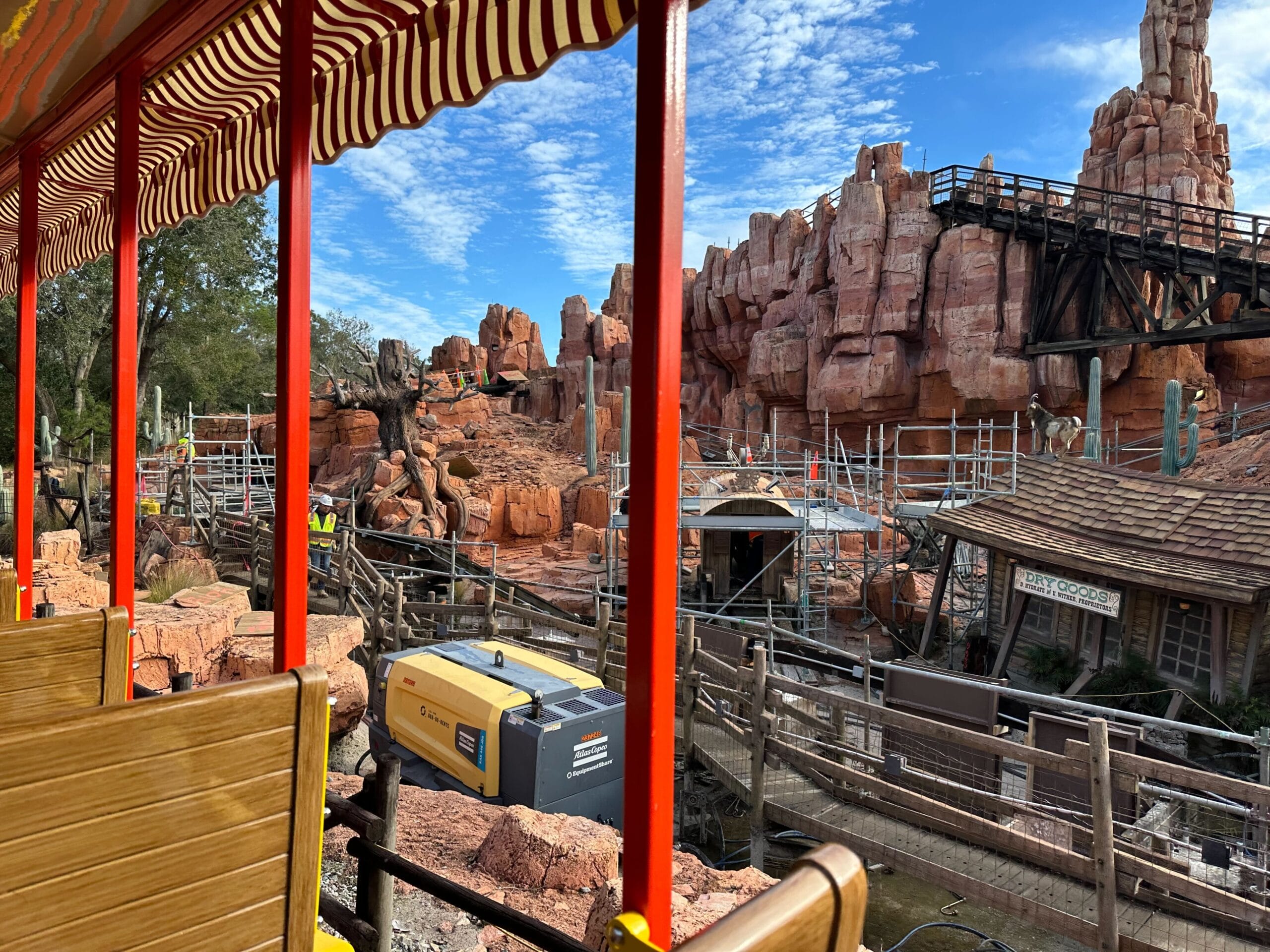 View from a train showing a construction site with red rock formations and scaffolding under a blue sky.