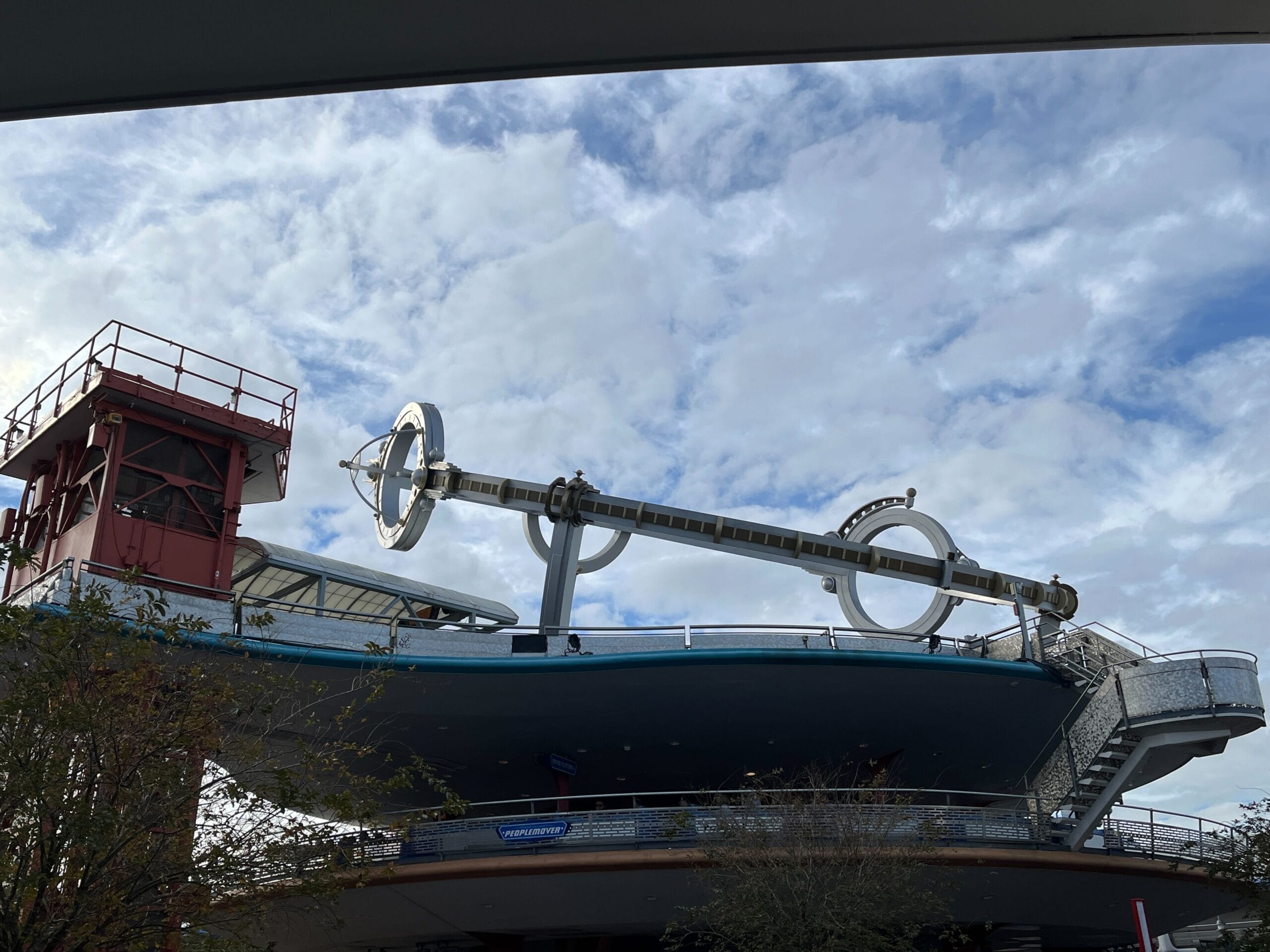 A refurbished structure featuring a large, metal armature with two circular elements reminiscent of the Astro Orbiter stands proudly on a rooftop against a cloudy sky.
