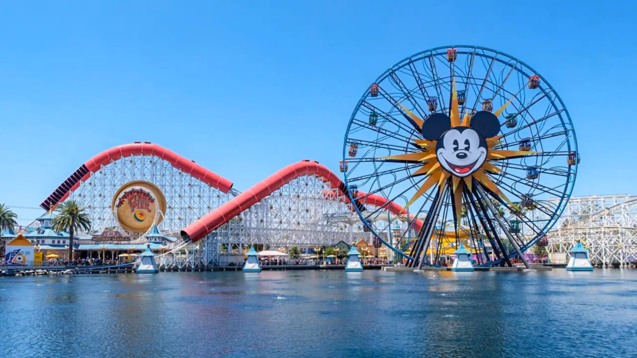 A large Ferris wheel with a Mickey Mouse face and red coaster in Paradise Gardens Park on a sunny day.