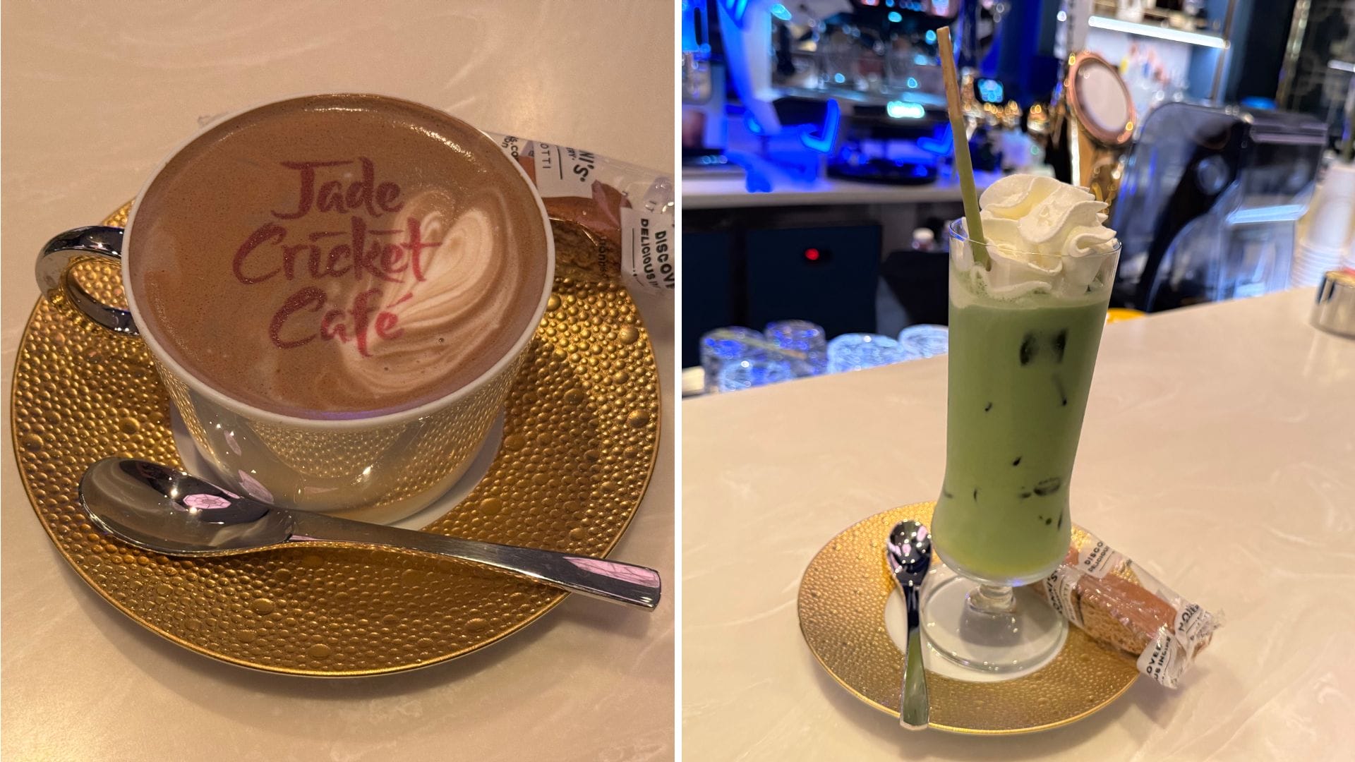 A cup of decorated hot chocolate and a green iced drink with whipped cream sit on a counter, each on gold saucers with a biscuit and a spoon.