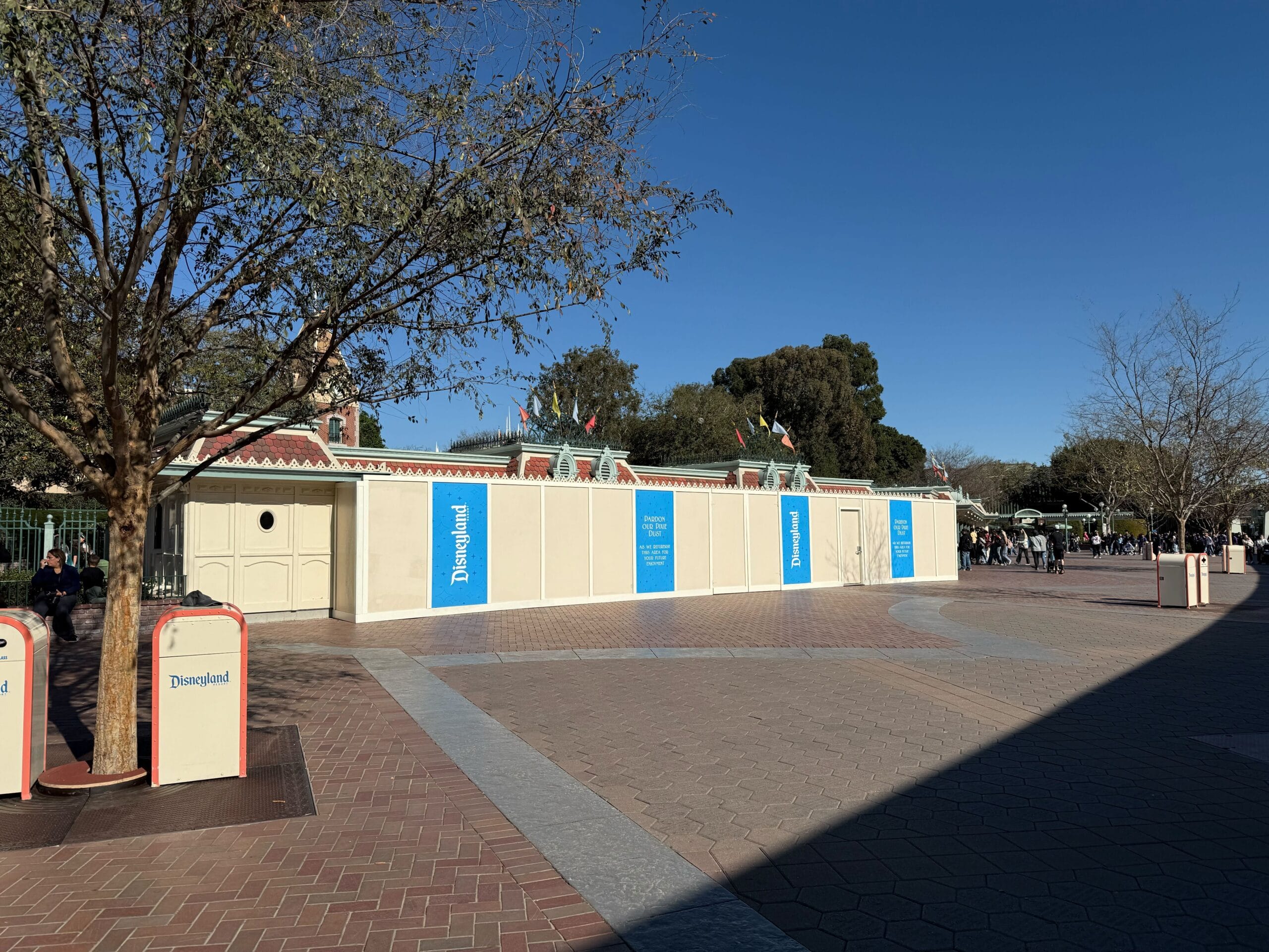 Construction walls surround an area at Disneyland. Trees and a clear blue sky are visible in the background.