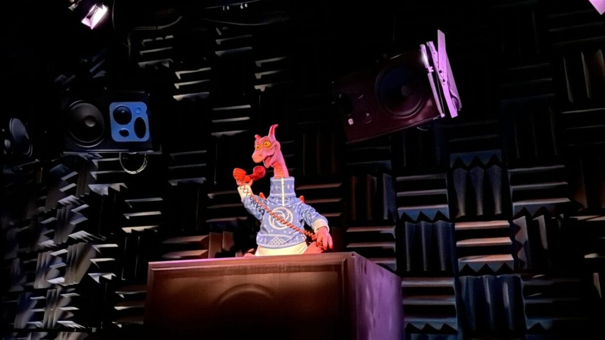 A red dragon puppet, Figment from Disney’s Journey Into Imagination, stands behind a desk in a soundproof room.
