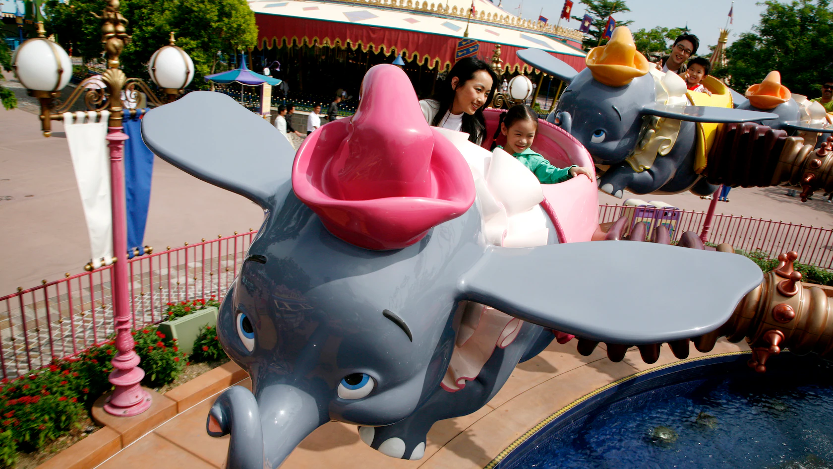 Parent and child revel on the Dumbo ride, soaring through the sky with flying elephants at an amusement park on a bright day.