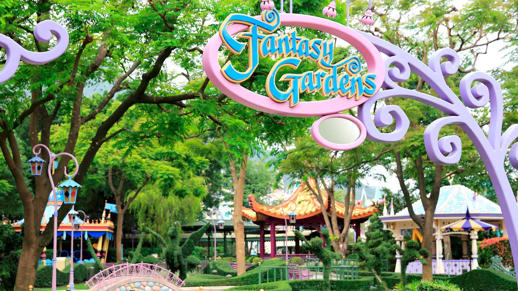 The entrance to Fantasy Gardens theme park is adorned with colorful signage and decorative structures, surrounded by lush trees and meticulously landscaped gardens that transport visitors into a whimsical fantasy.