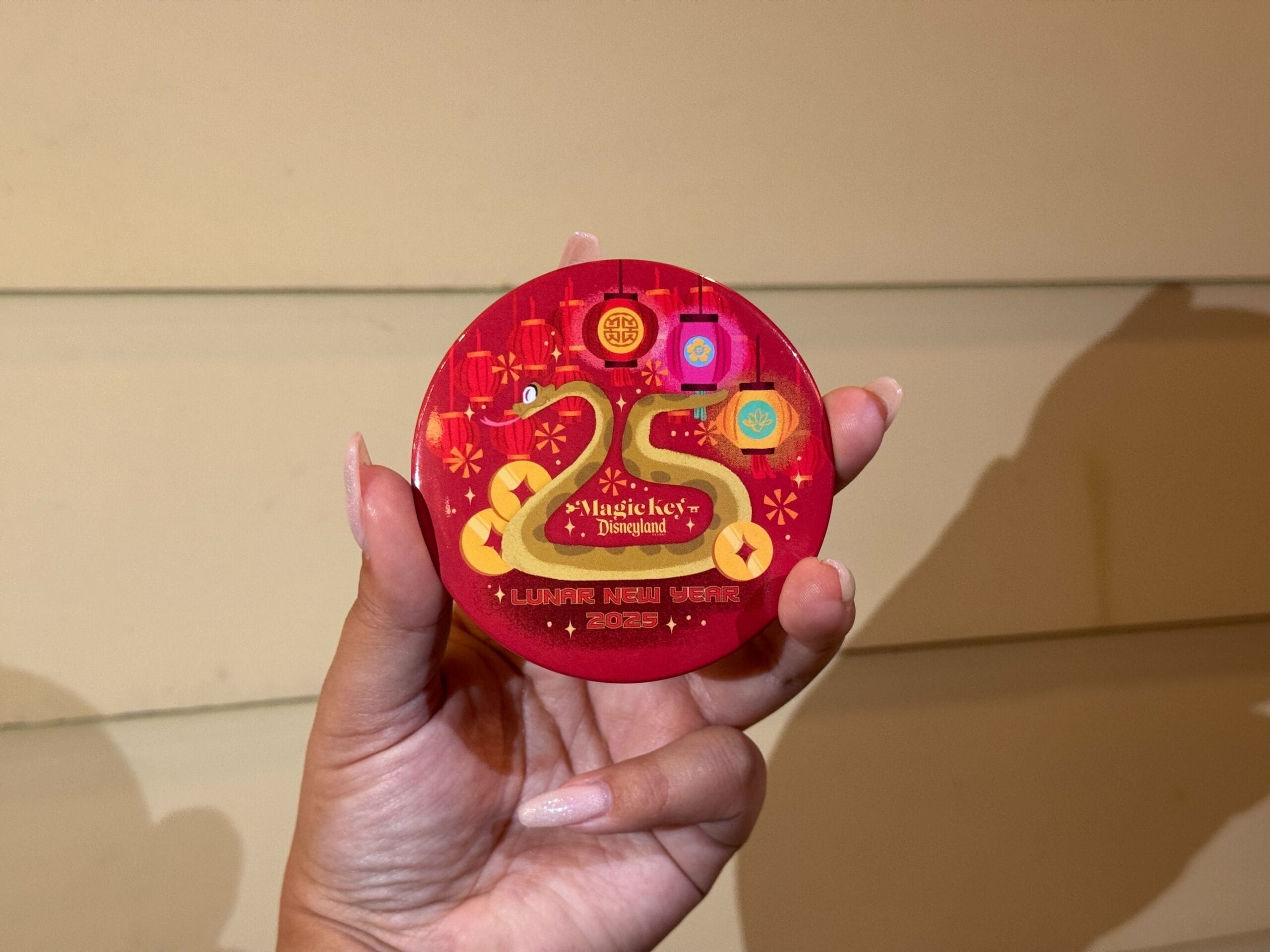 A hand holds a red circular badge adorned with "25 Years" and "Lunar New Year 2023" in gold and yellow accents, reminiscent of the vibrant celebrations at Disney California Adventure.