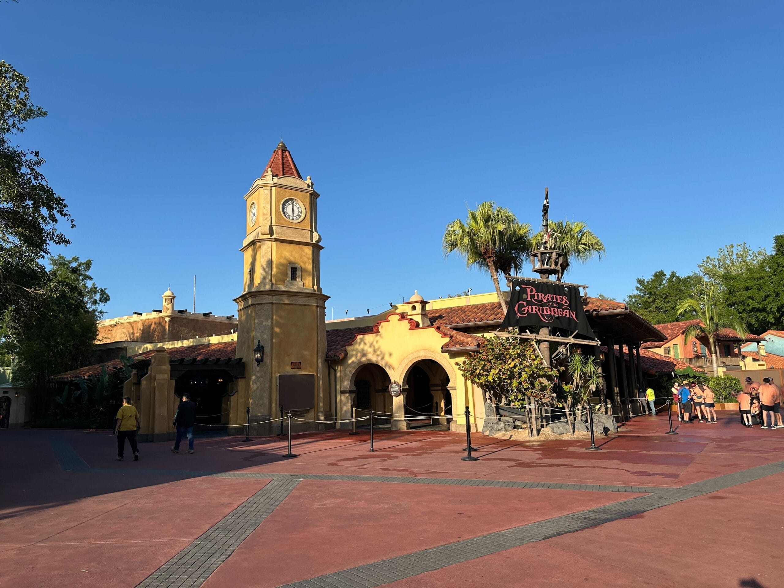 Yellow clock tower at the Pirates of the Caribbean attraction entrance under a clear blue sky.
