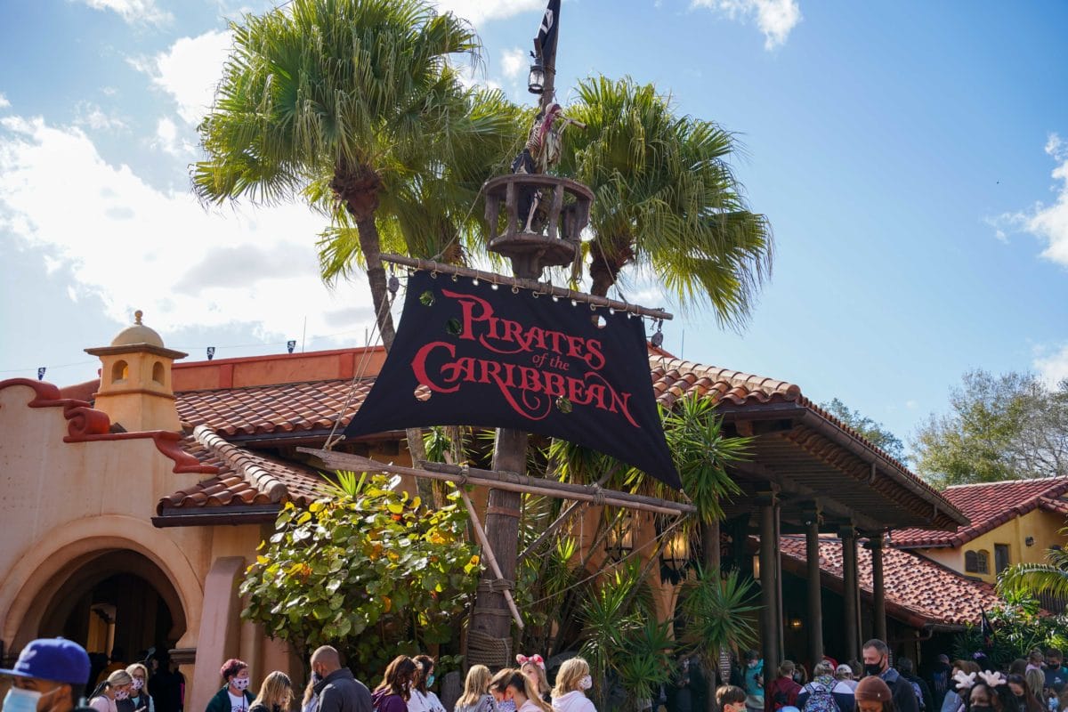 Pirates of the Caribbean ride entrance sign draws a crowd beneath swaying palm trees at the theme park.