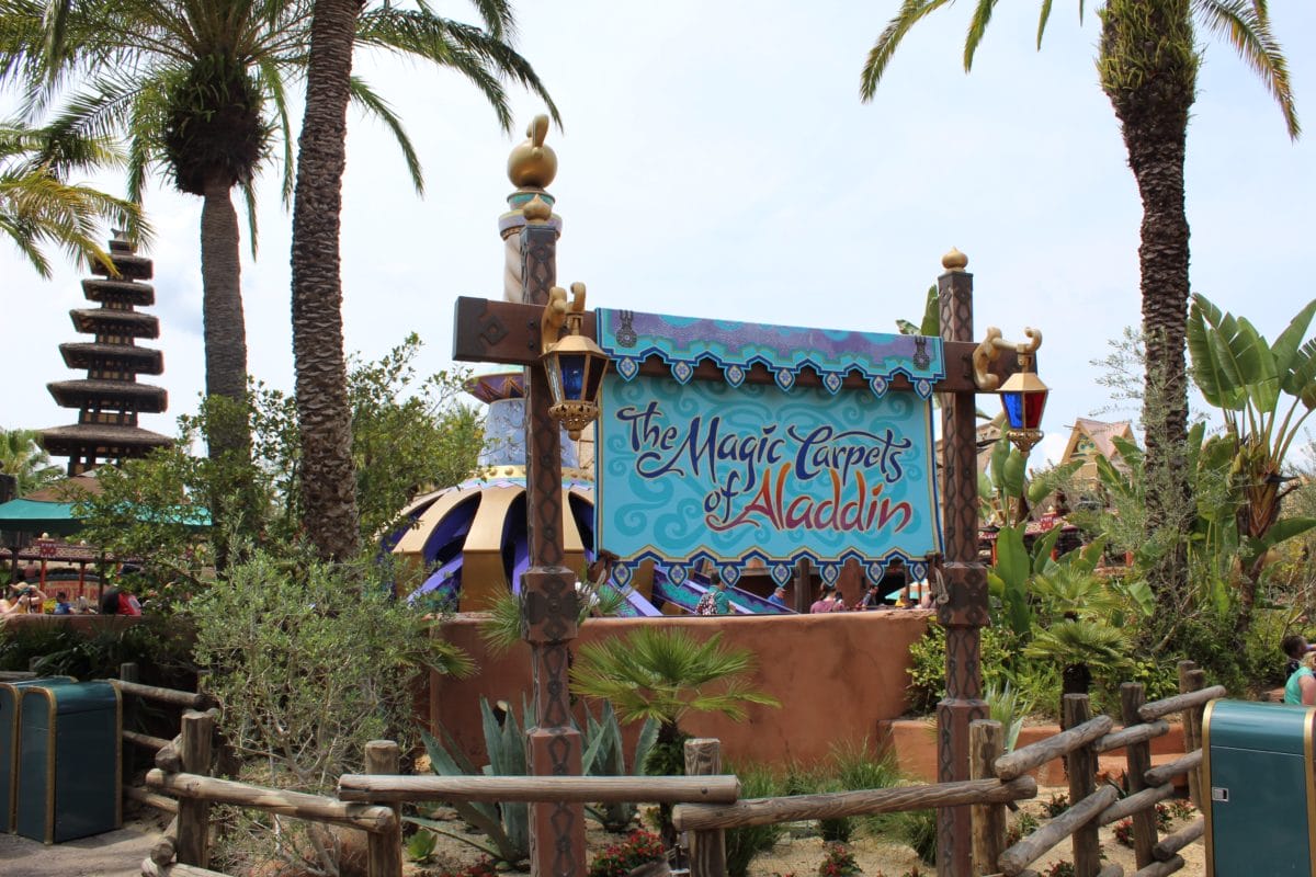 Entrance sign for the Aladdin ride, The Magic Carpets of Aladdin, amid palm trees and lush greenery at this Disney attraction.
