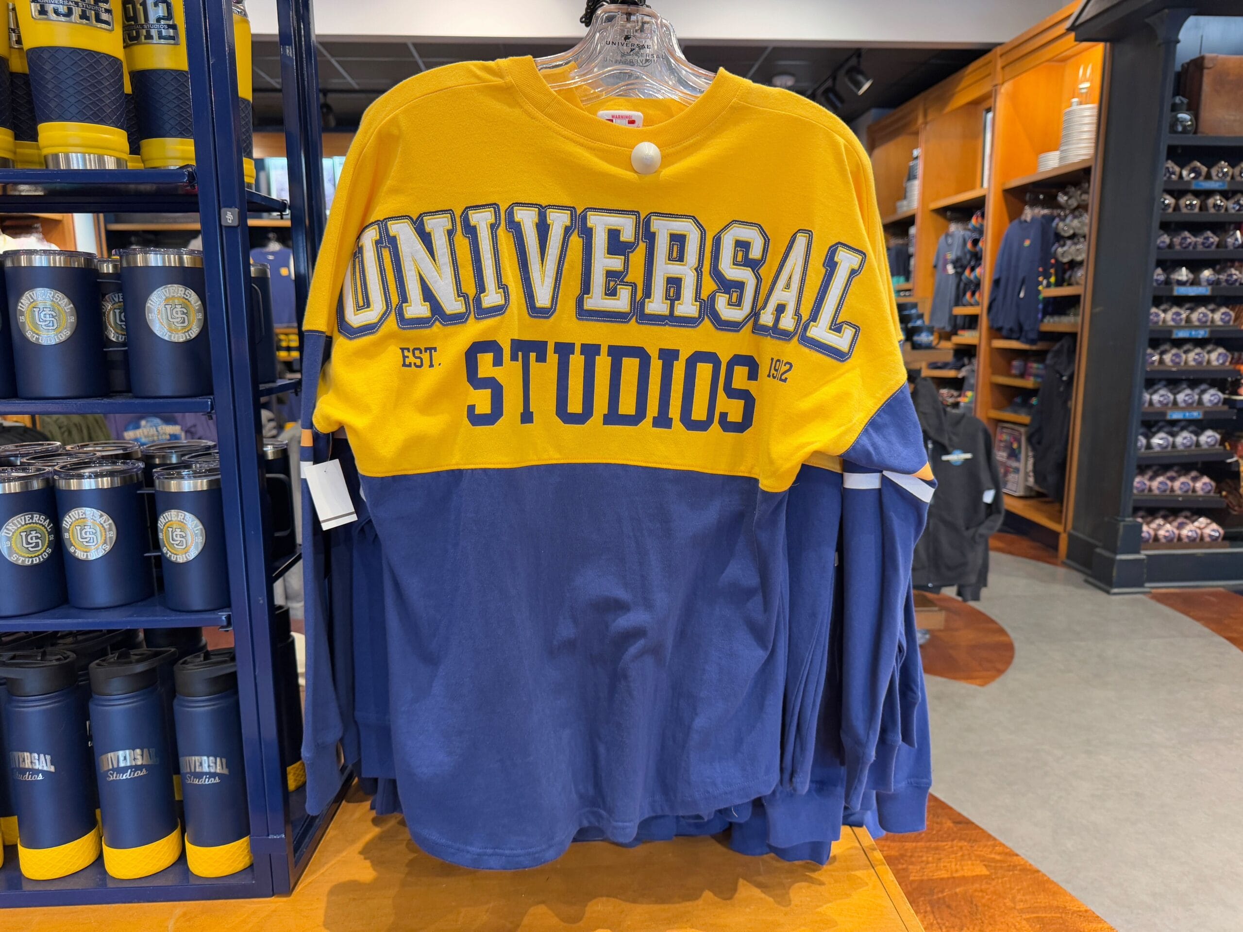 Yellow and blue Universal Studios long-sleeve shirt on display, surrounded by themed merchandise in a store.
