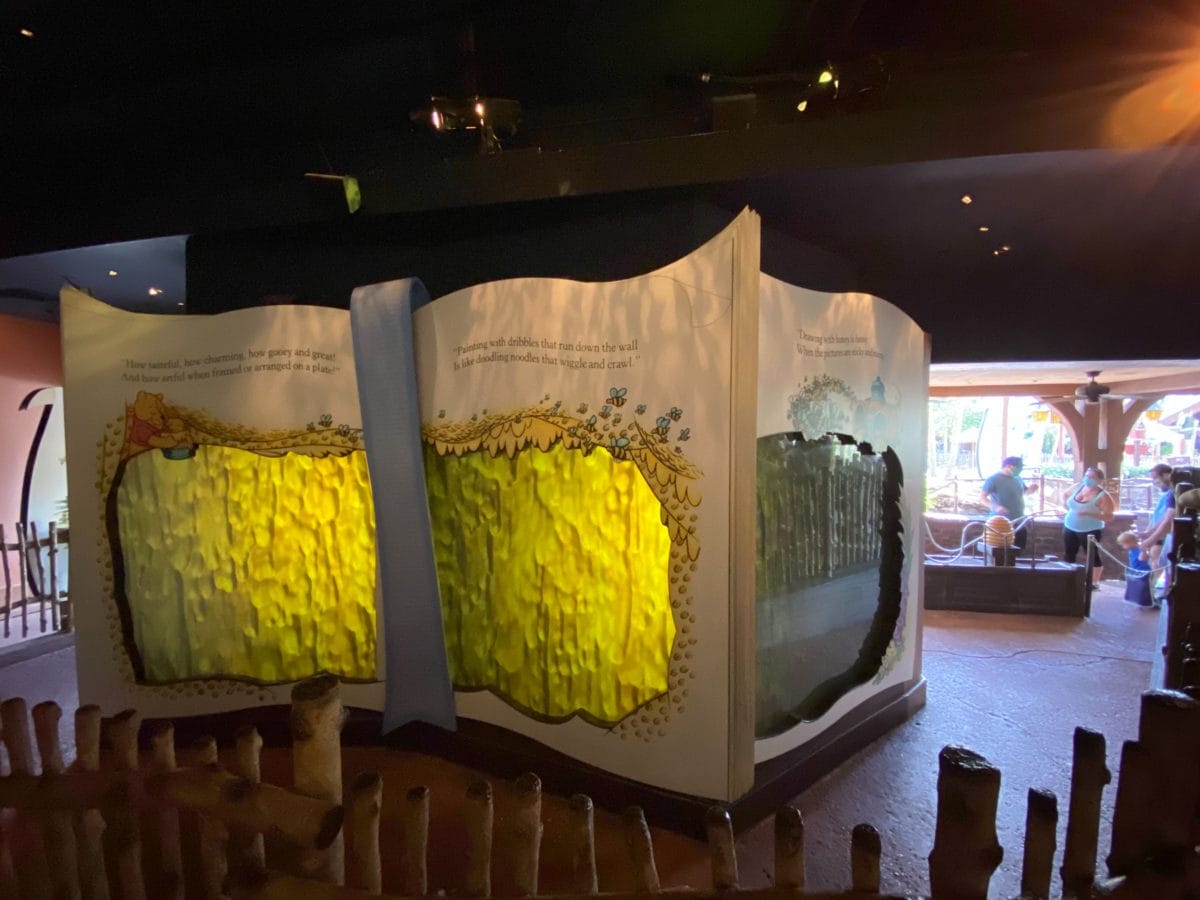 Large storybook display with yellow and green interactive panels from The Many Adventures of Winnie the Pooh in a dim room.
