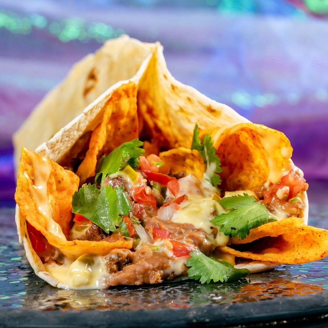 A burrito filled with chips, melted cheese, beans, salsa, and cilantro on a textured surface.