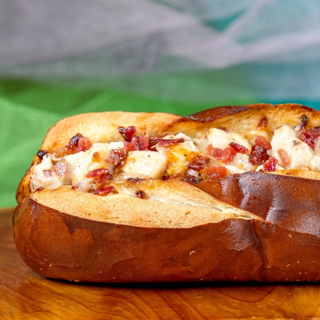 A bread loaf stuffed with melted cheese and diced bacon, placed on a wooden surface.