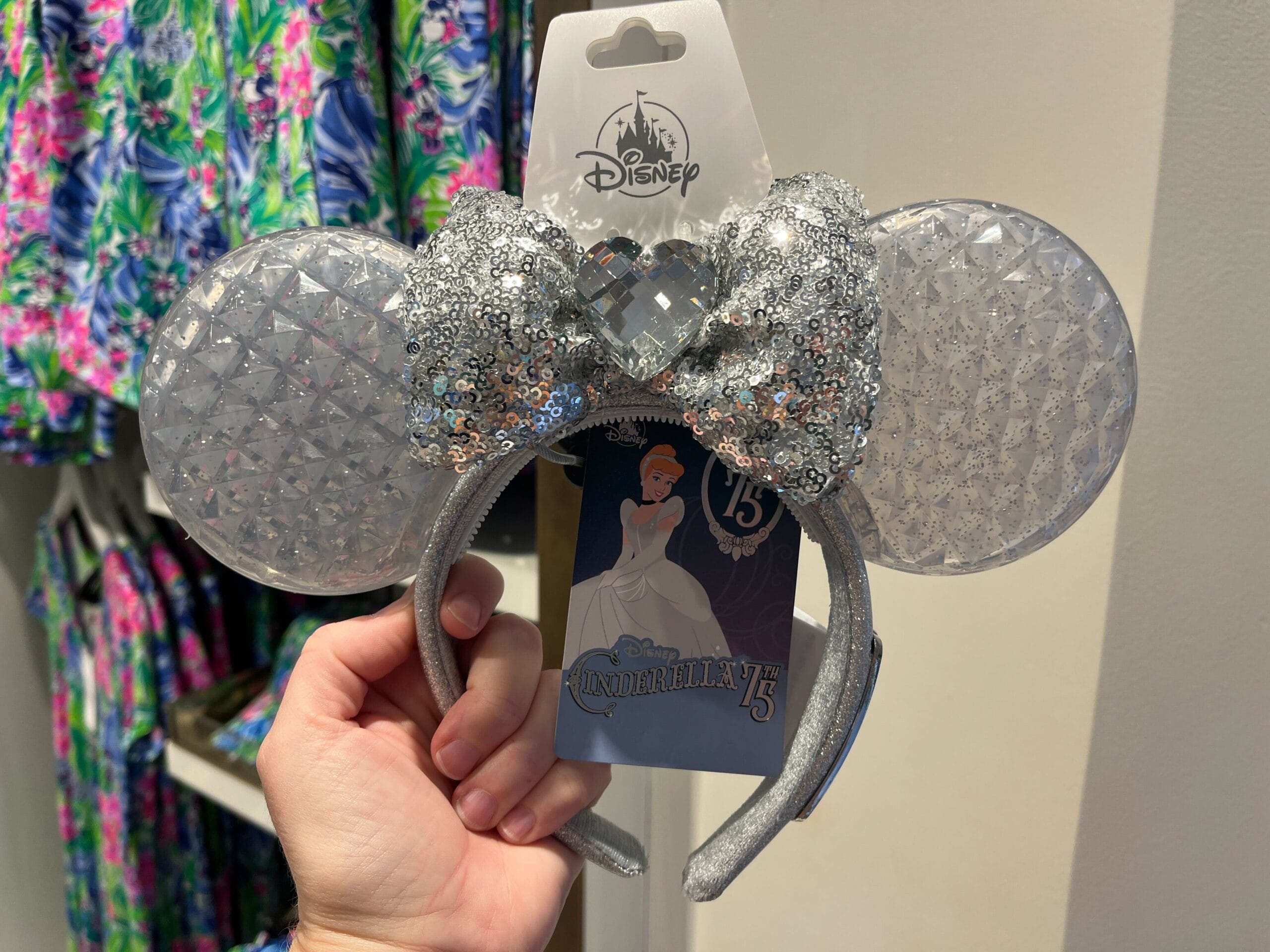 A hand displays a shimmering silver sequined Minnie Mouse ear headband adorned with a Cinderella 75th Anniversary tag, capturing the magic of Walt Disney World in this enchanting store display.