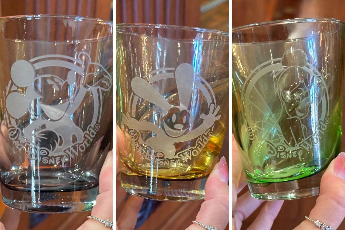 Three glass tumblers from the Crystal Arts shop, etched with Disney World designs of different characters, each showcasing a unique color tint: black, yellow, and green.