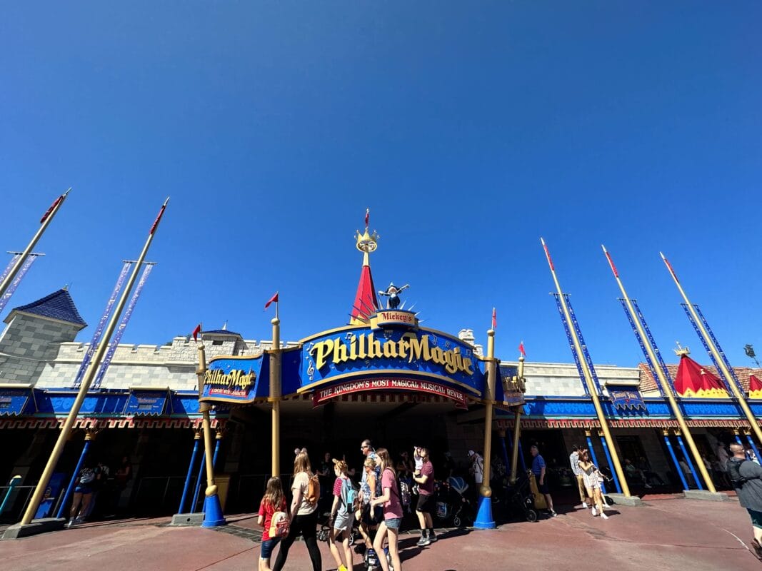 Guests stroll past Mickey's PhilharMagic, a dazzling Disney attraction under a clear blue sky.