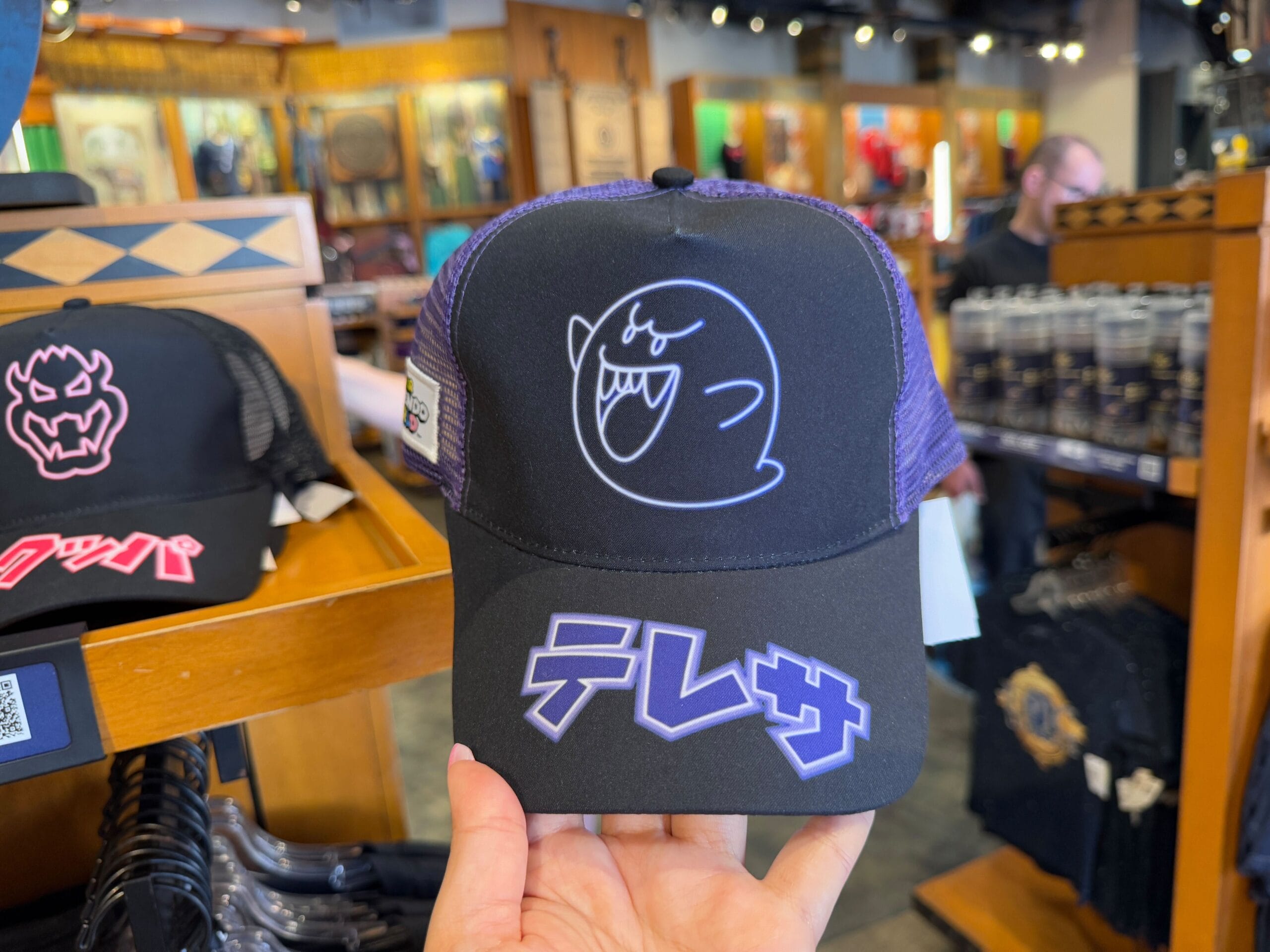 A black hat with a neon blue ghost design and Japanese text on the front, showcased as part of the NEW Epic Universe merchandise at Universal Studios Florida.