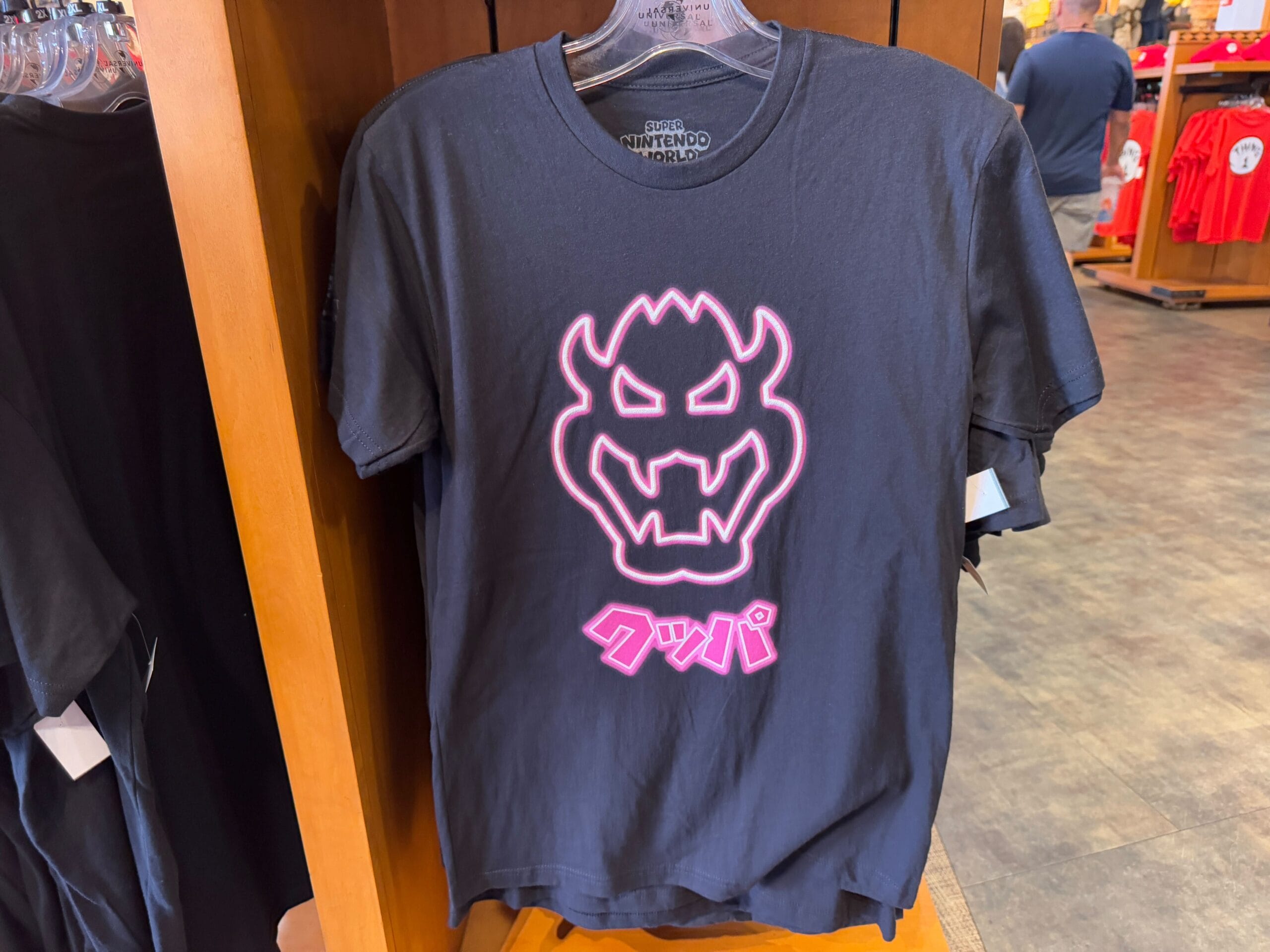 Black T-shirt with neon pink graphic of a stylized face and Japanese text, available as part of the Epic Universe Merchandise collection at Universal Studios Florida.