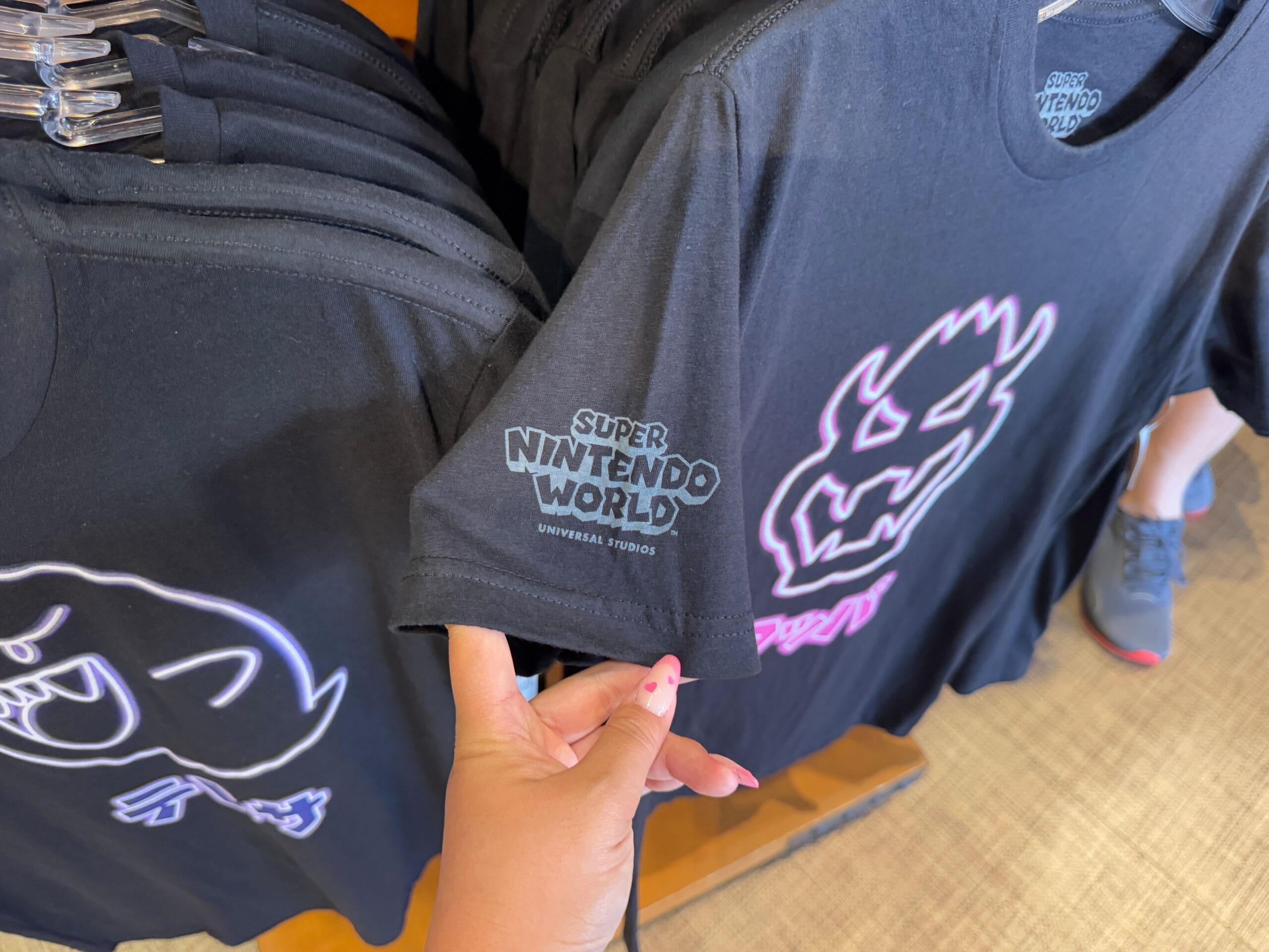 A person holds a new Super Nintendo World T-shirt from the Epic Universe Merchandise collection, featuring a glowing outline design.