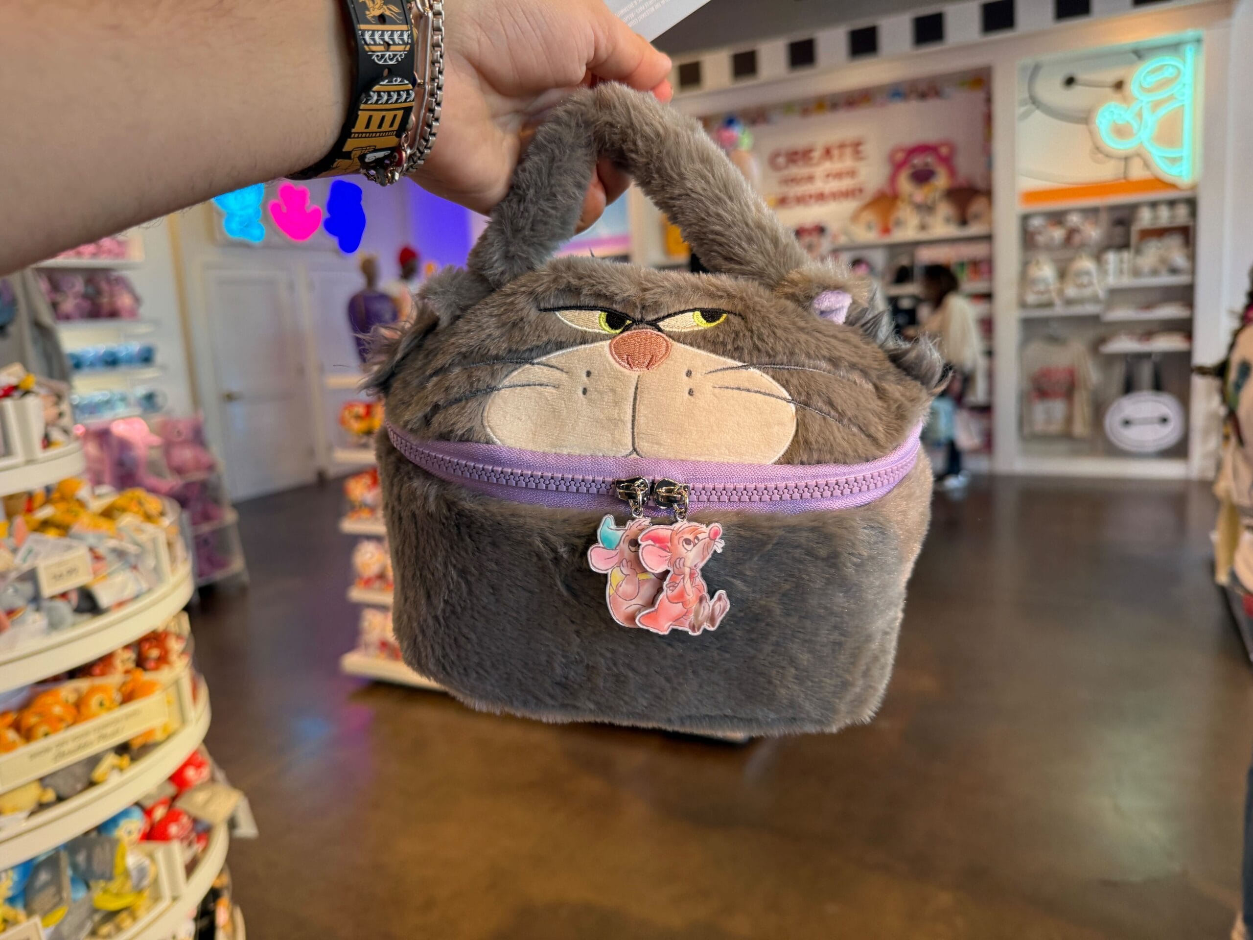 In a store brimming with plush toys and merchandise, a person holds a gray cat-shaped plush bag reminiscent of a Disney magic, complete with a zip and cartoon character charm, evoking the whimsical spirit of the Disneyland Resort.