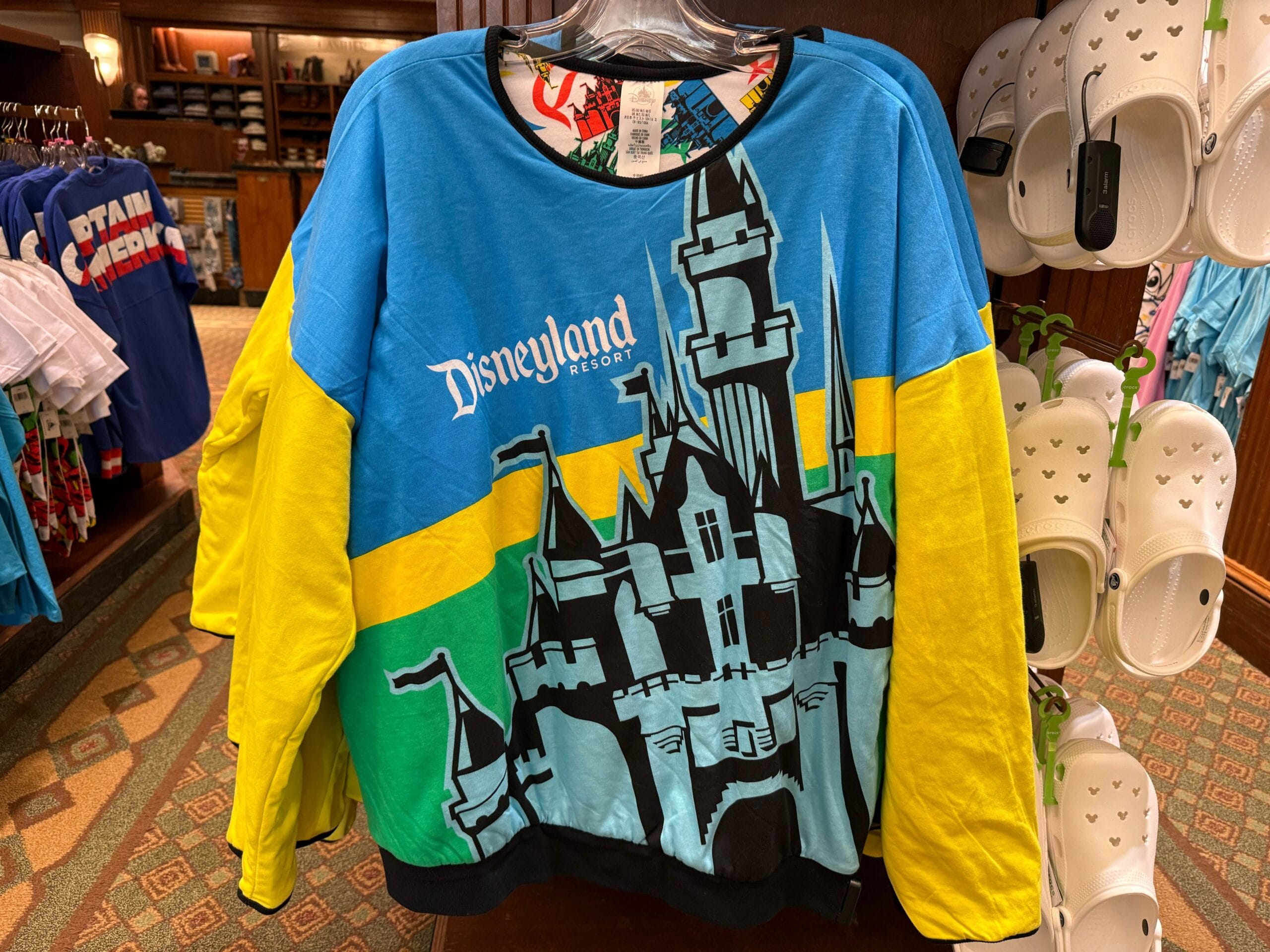 Colorful Disneyland sweatshirt with a castle graphic displayed on a rack, alongside white Crocs sandals.