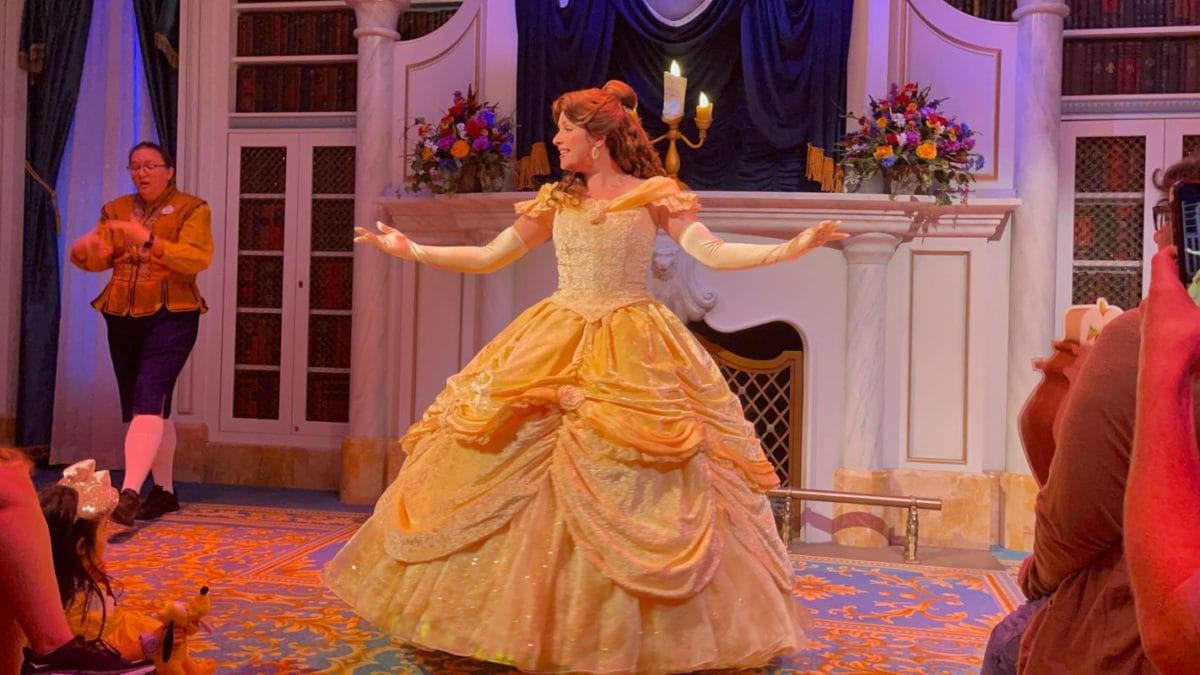 Woman dressed as Disney’s Belle dances on stage in a yellow gown as the audience enjoys these Enchanted Tales.