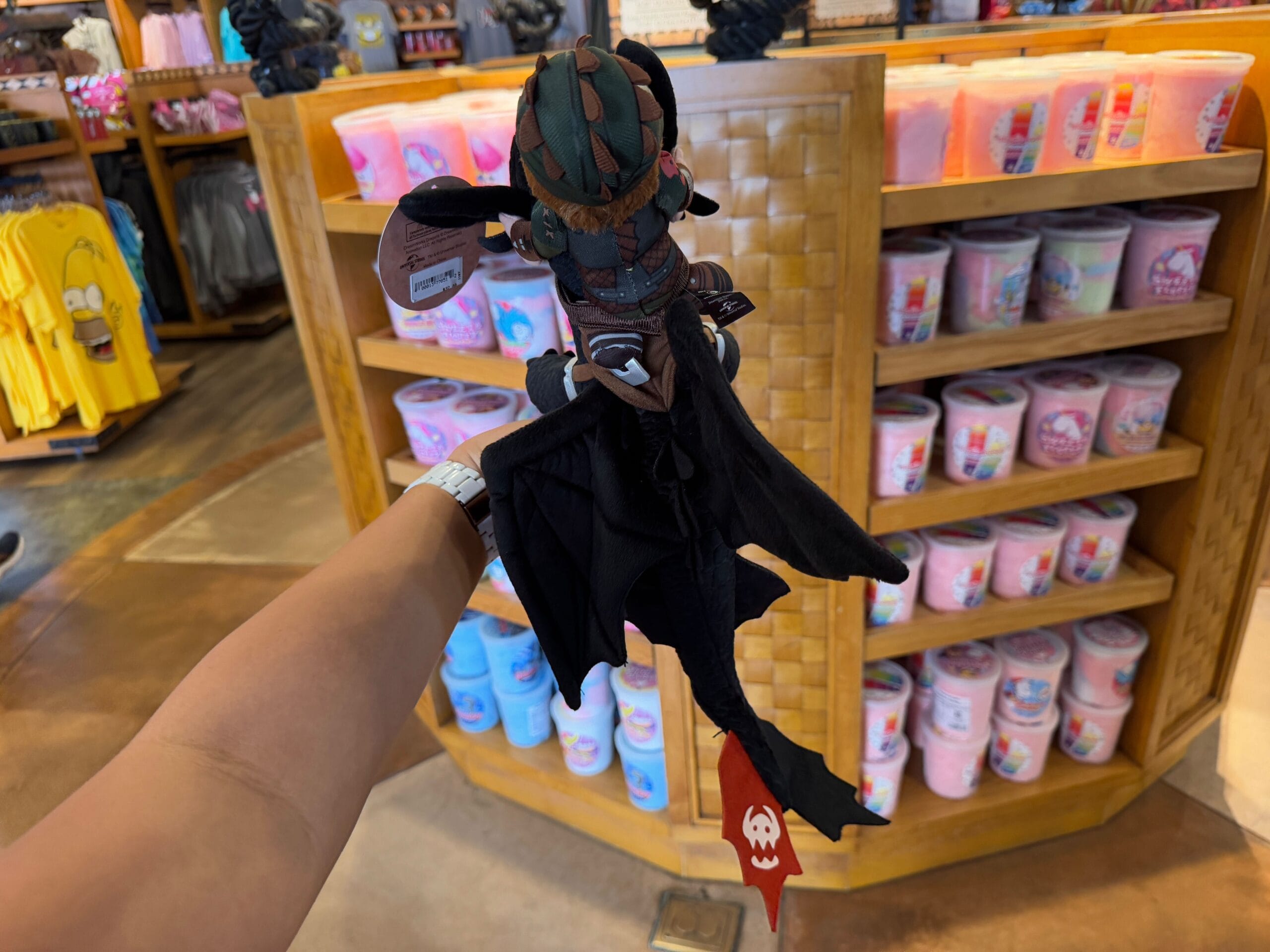A plush dragon toy from the Epic Universe Merchandise collection is showcased against a vibrant cotton candy display in a store, capturing the whimsical charm reminiscent of Universal Studios Florida.