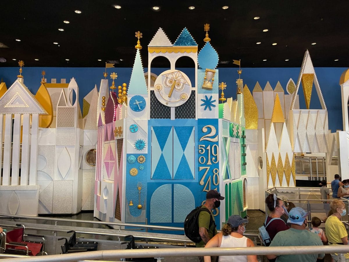 People wait in line before the colorful geometric facade of the small world attraction at a theme park.