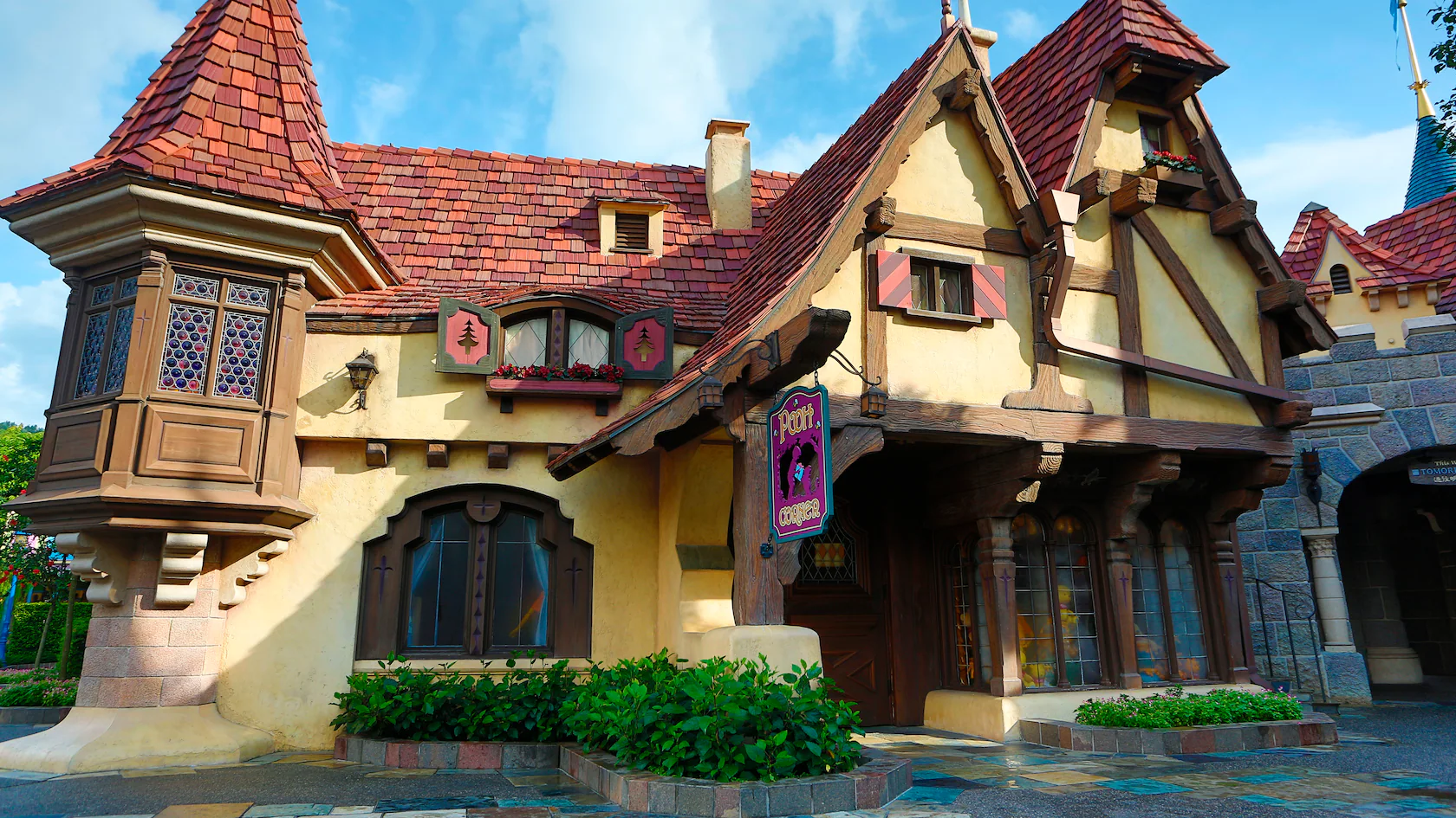 A whimsical cottage with a red-tiled roof, timber accents, and stained glass windows under a blue sky. A vine grows near the entrance.