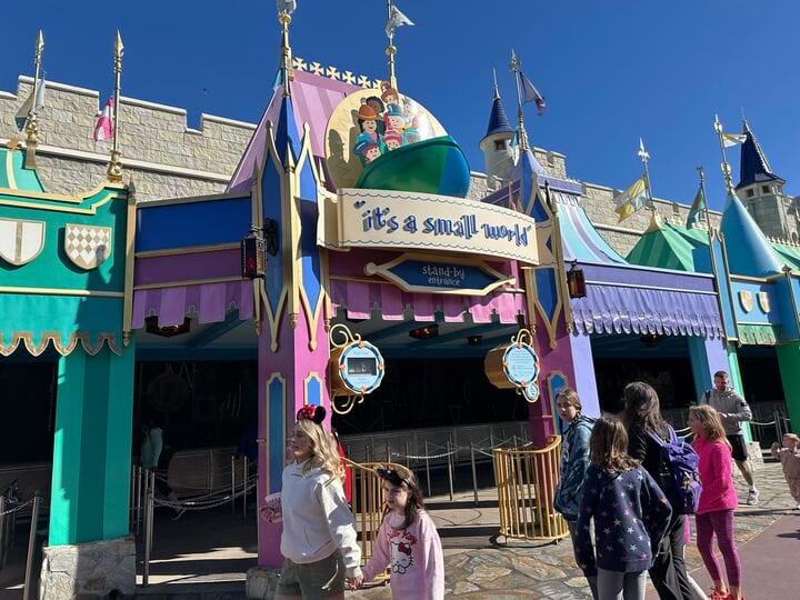 Visitors gather near the entrance of the enchanting "It's a Small World" ride at Walt Disney World, surrounded by colorful banners and castle-like architecture, capturing the magic of this iconic attraction.