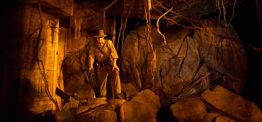 In explorer attire, a person stands in a dimly lit cave reminiscent of the Indiana Jones Adventure, surrounded by rocks and vines. A large boulder looms in the background, reminiscent of the thrilling scenes you might find at Tokyo DisneySea after a magical refurbishment.