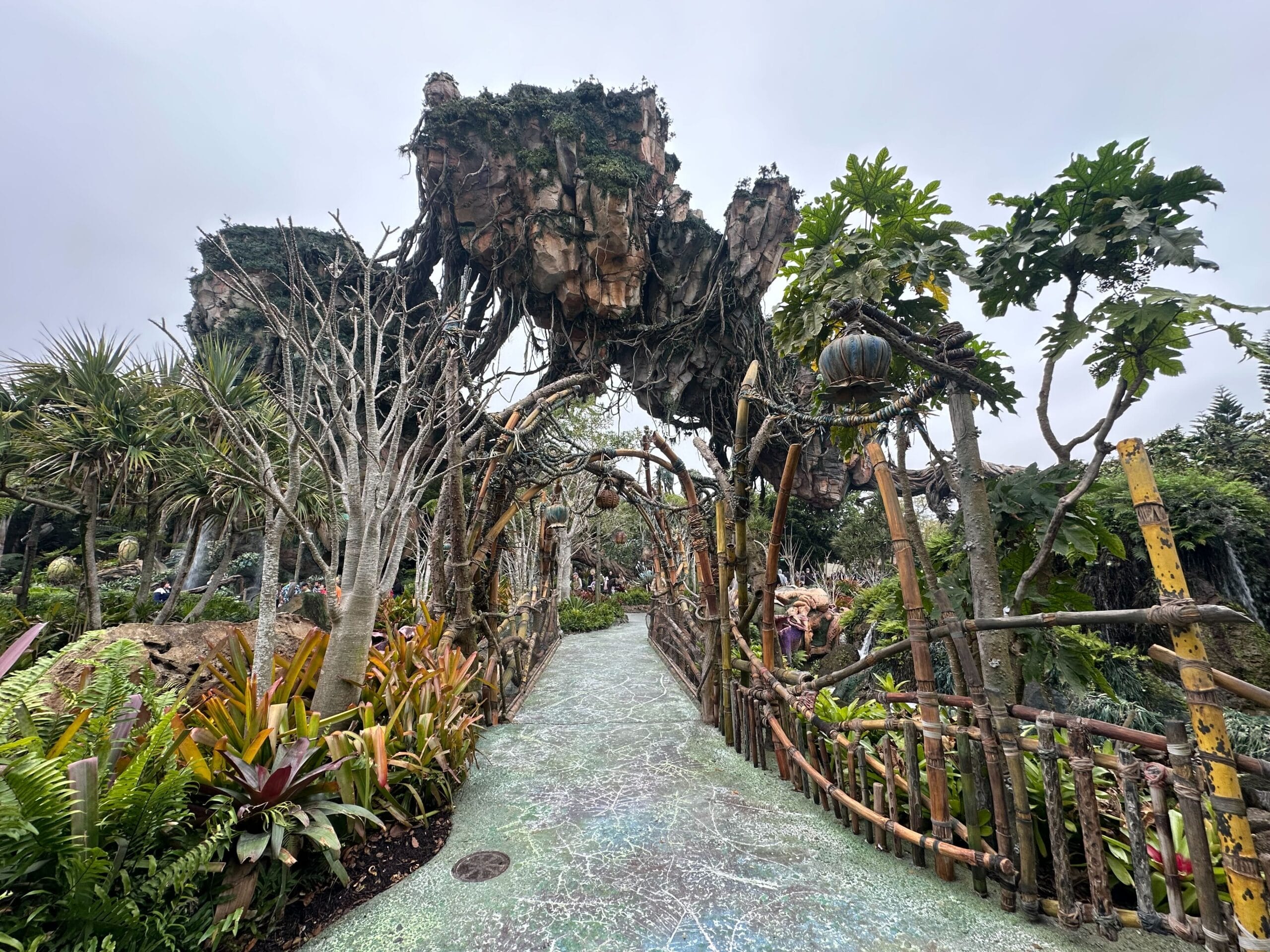 Pathway surrounded by lush plants leads to towering floating rock structures, reminiscent of a fantasy landscape.