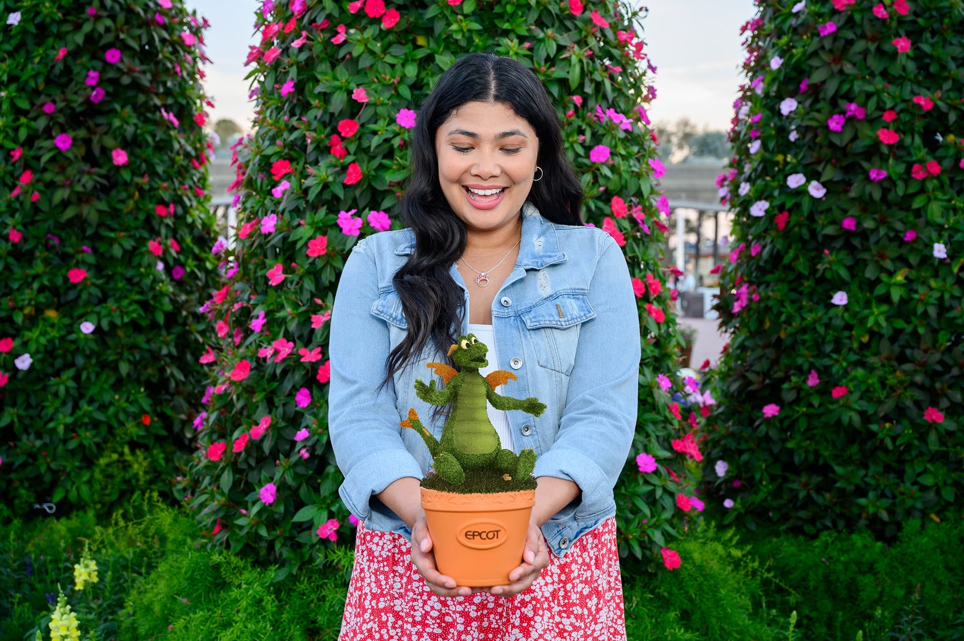 At the 2025 EPCOT Flower & Garden Festival, a woman holds a small potted plant shaped like a dragon, standing proudly among the large flower-covered structures.