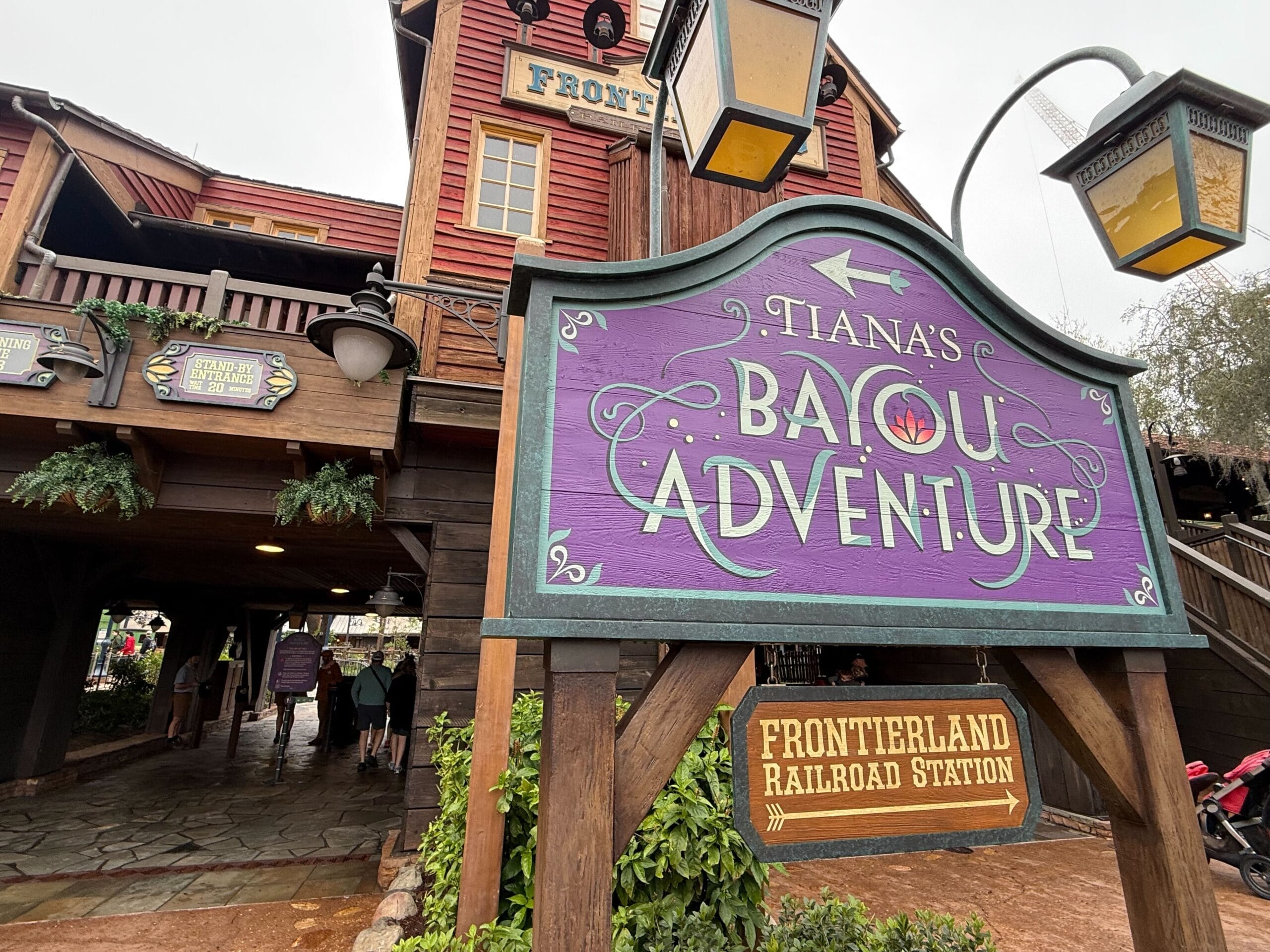 Entrance sign for "Tiana's Bayou Adventure" near Frontierland Railroad Station, featuring rustic wooden architecture and hanging lanterns.