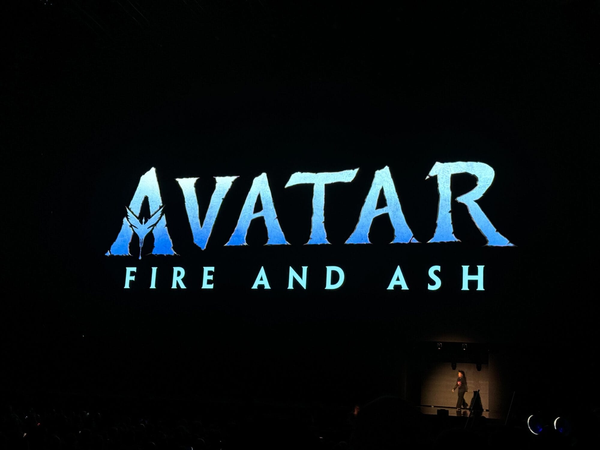 A large screen showcasing "Avatar: Fire and Ash" looms over the stage, casting dramatic shadows of a silhouetted figure below, embodying the great ideas woven into this cinematic masterpiece.