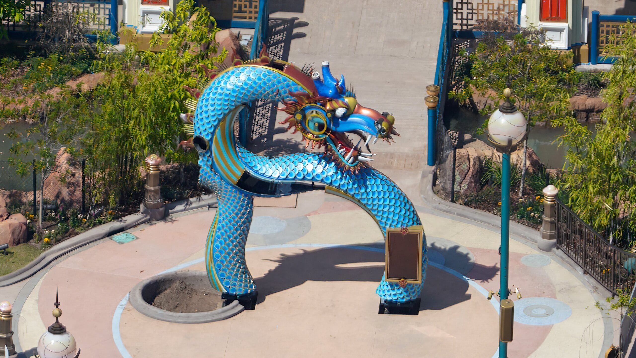A colorful Blue Dragon Archway with a fierce expression and intricate blue scales stands proudly outdoors, surrounded by lush greenery and winding pathways.