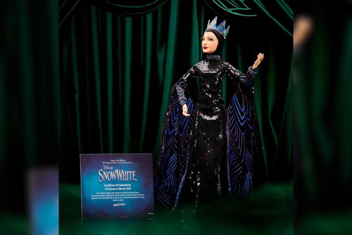 A Gal Gadot Evil Queen doll, elegantly dressed in a black and silver gown with a crown, stands proudly beside a Disney Snow White certificate against an enchanting dark green curtain backdrop.