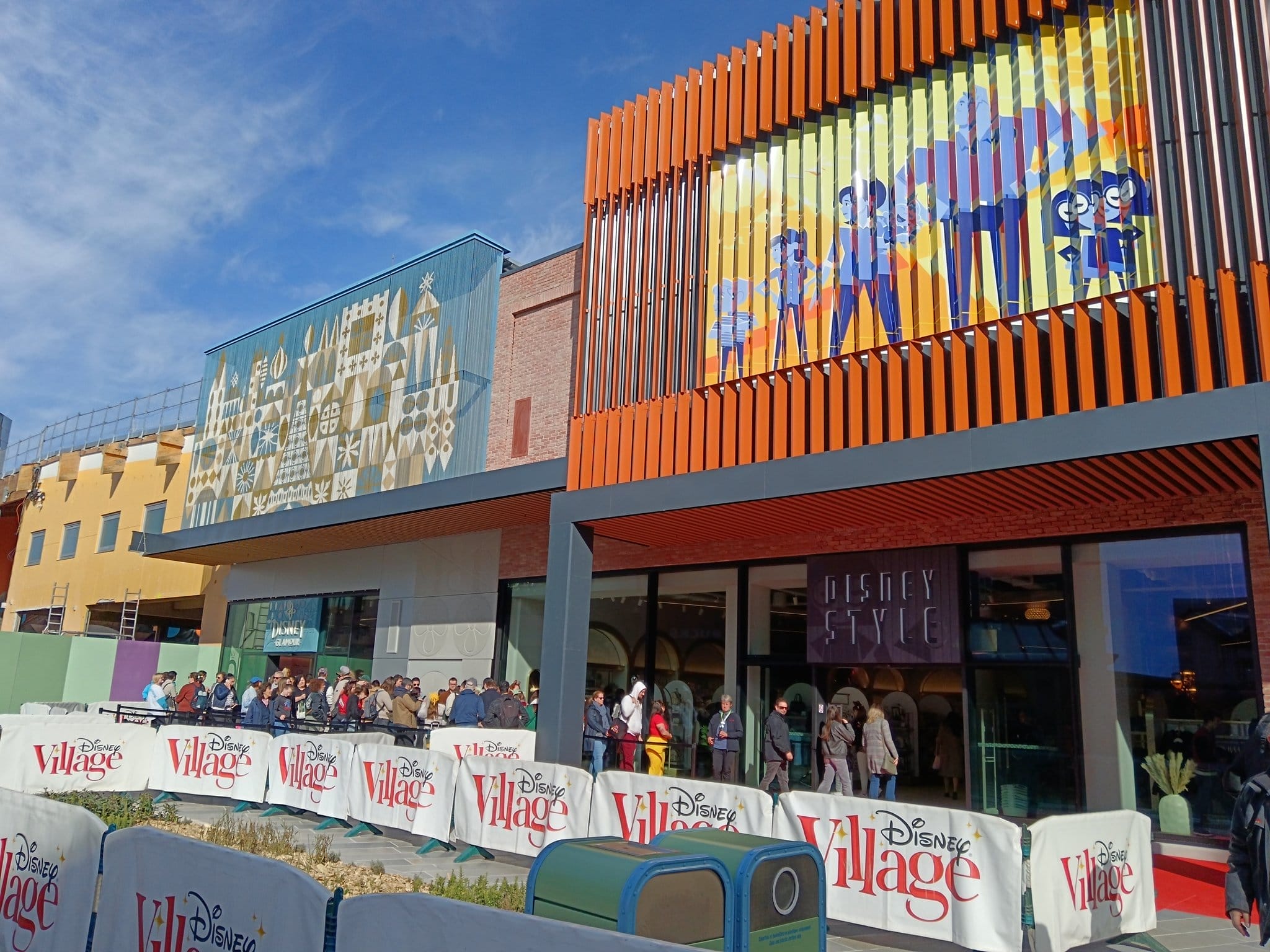 People lined up outside Disney Style at Disney Village, with colorful murals against the building's facade under a clear blue sky, capturing the magic of Disneyland Paris.