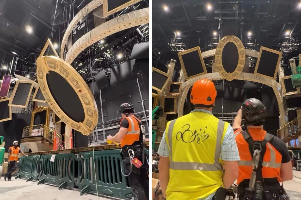 Workers in safety gear set up a large, ornate stage frame with multiple cutouts. One worker gestures towards the frame, discussing the arrangement in a theater setting.