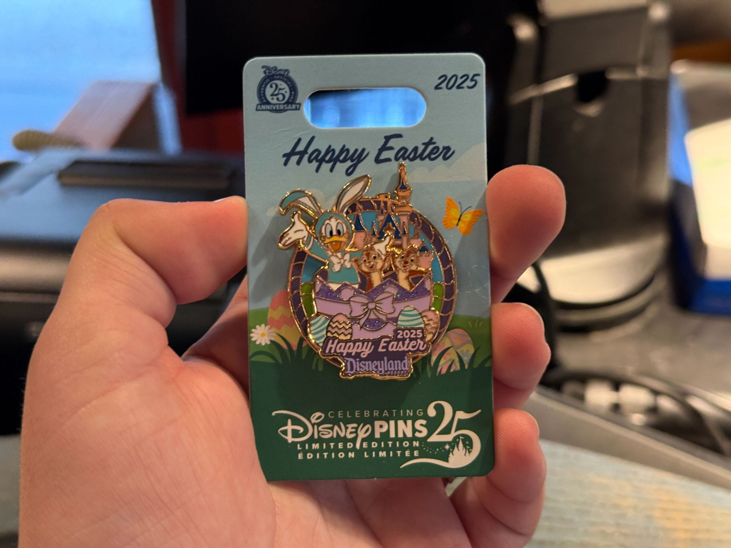 A person proudly displays a Disneyland Resort collectible pin celebrating "Happy Easter 2025," featuring beloved characters in festive attire, marked as the 25th edition.