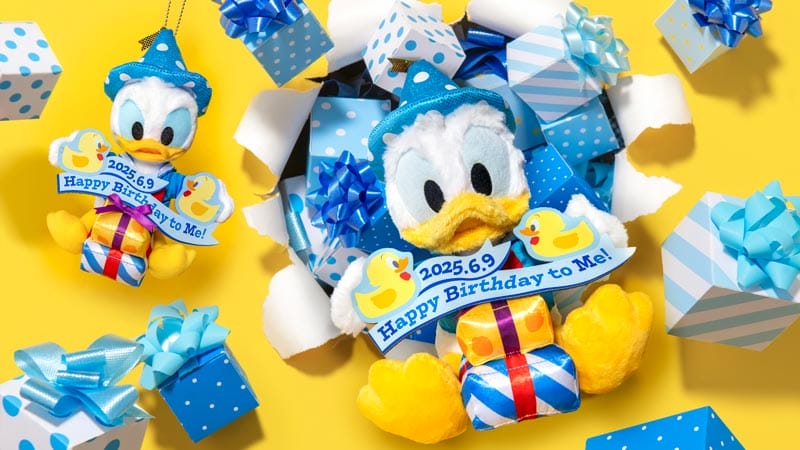 A plush cartoon duck with a blue hat holds a "Happy Birthday to Me!" sign, surrounded by blue polka dot gift boxes and bows on a yellow background. It's a perfect piece of Donald's Birthday Merchandise straight from Tokyo Disneyland!.