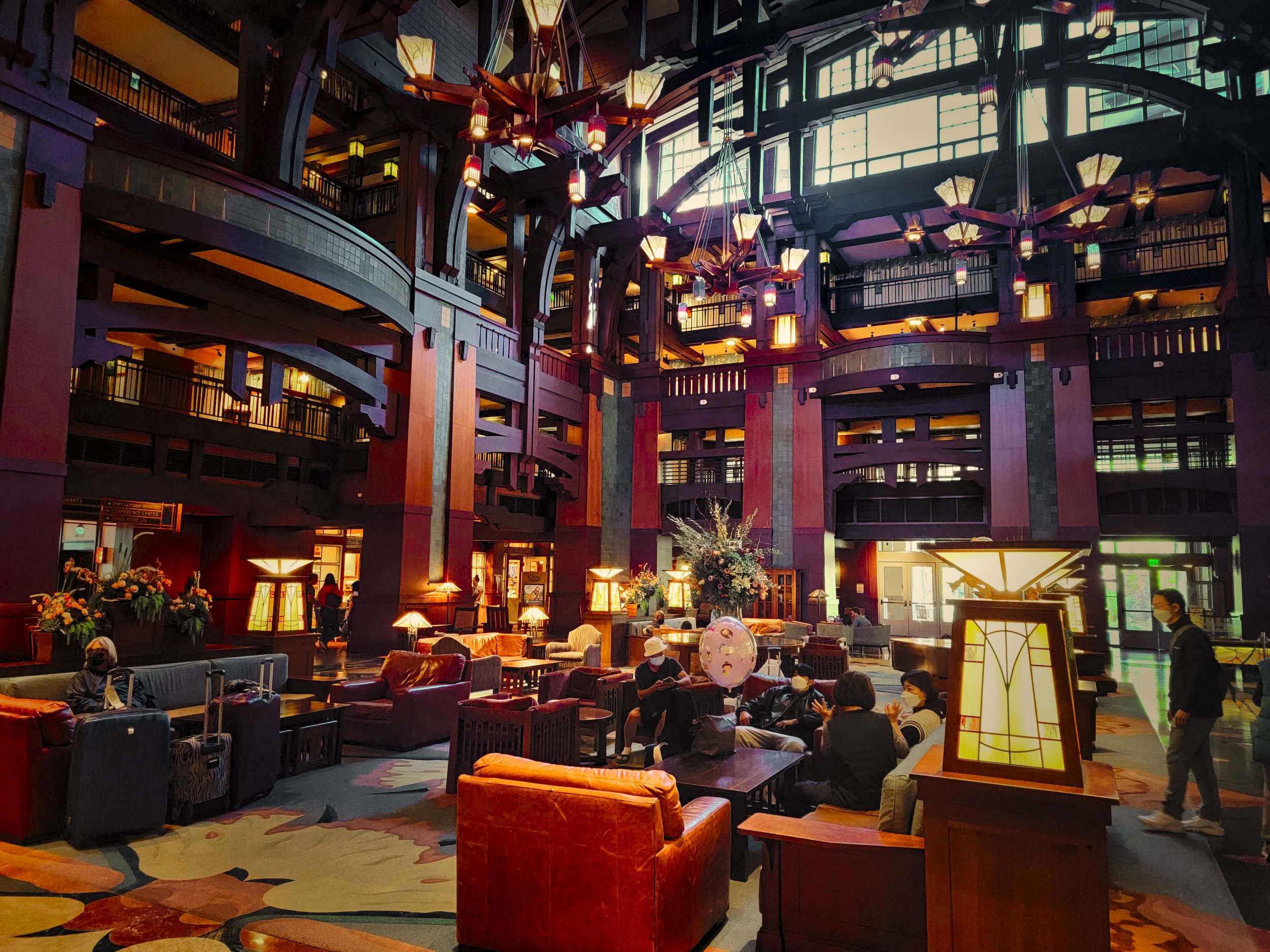 The grand lobby of the Grand Californian Hotel boasts high ceilings, wooden beams, and ornate lighting. Various seating areas invite guests to relax and soak in the luxurious ambiance.
