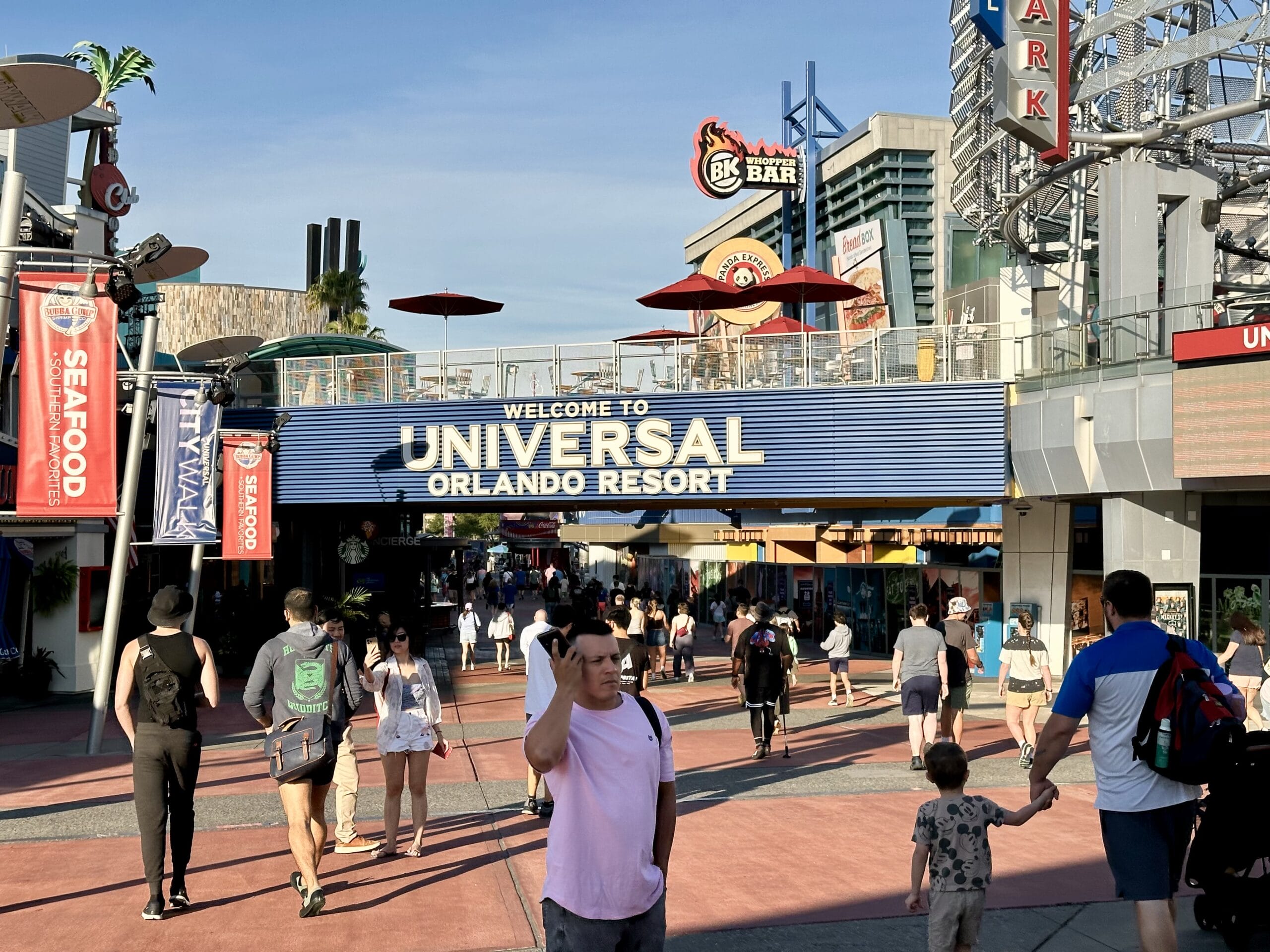 People strolling beneath the iconic "Welcome to Universal Orlando Resort" sign find themselves amidst a vibrant scene of restaurants and attractions, all in anticipation of the upcoming EPIC Universe expansion.