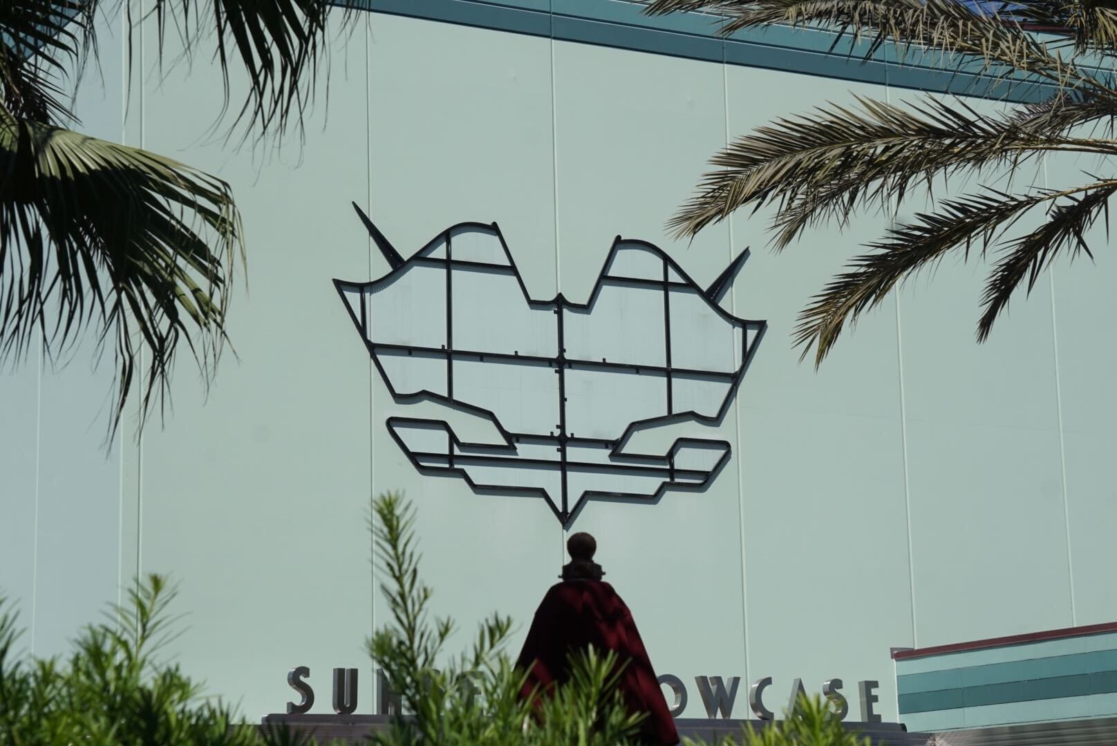 A large geometric cat-shaped art piece is mounted on a light green wall, with "Sunset Showcase" partially visible below, flanked by palm trees and greenery—a true Hollywood Studios vibe.