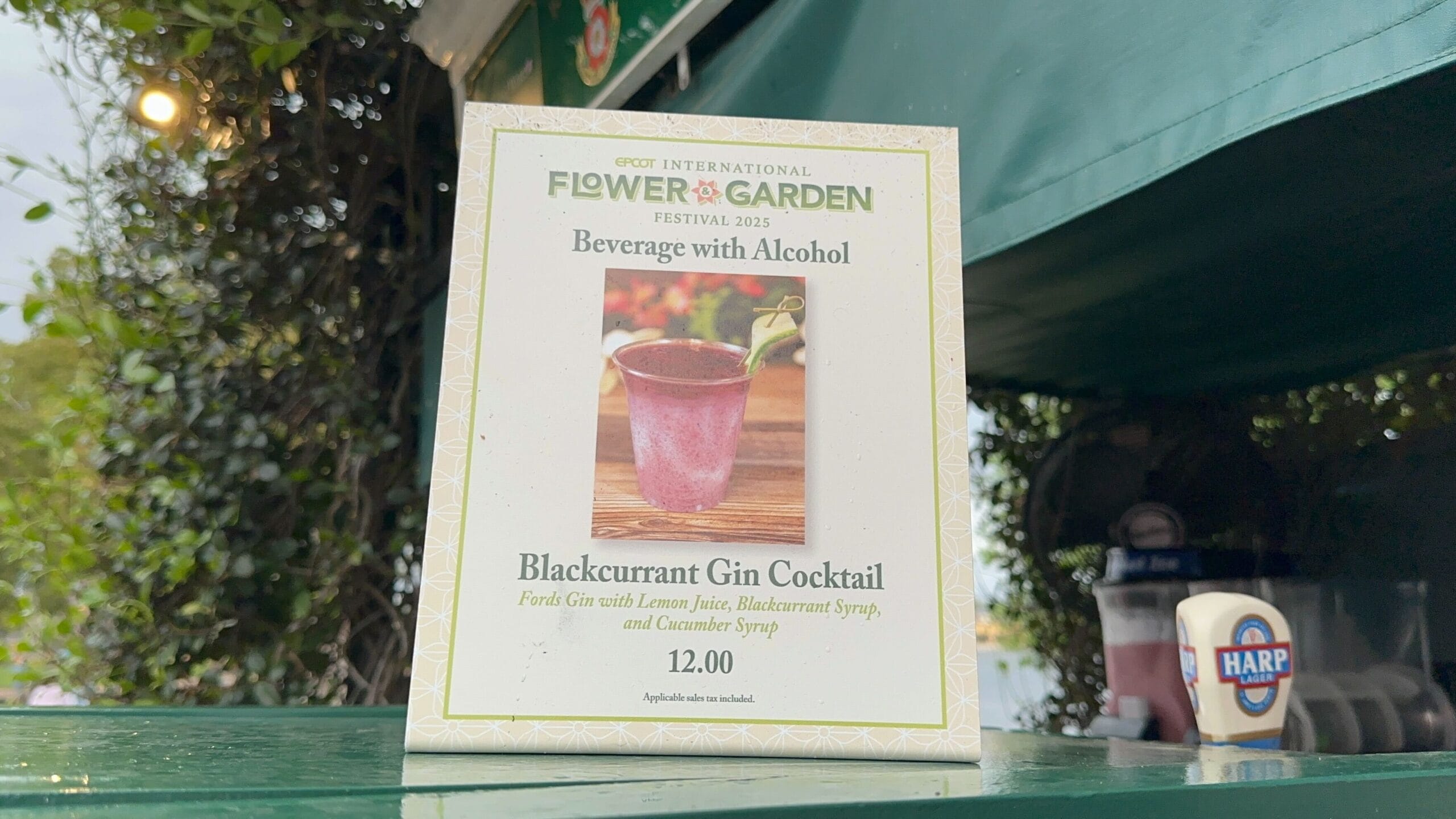 A sign at the Flower & Garden Festival showcases a refreshing Blackcurrant Gin Cocktail, available for $12.00 at the Epcot International.