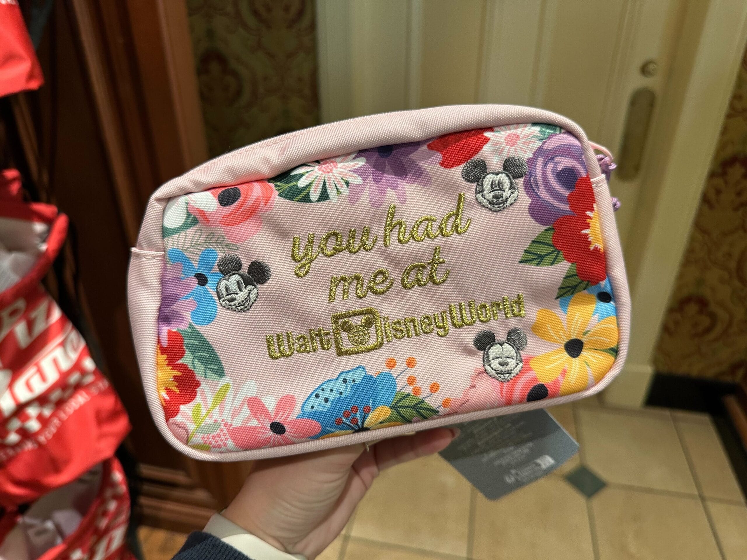 A pink pouch with Mickey Mouse designs and floral patterns, featuring the text "you had me at Walt Disney World" in gold lettering.