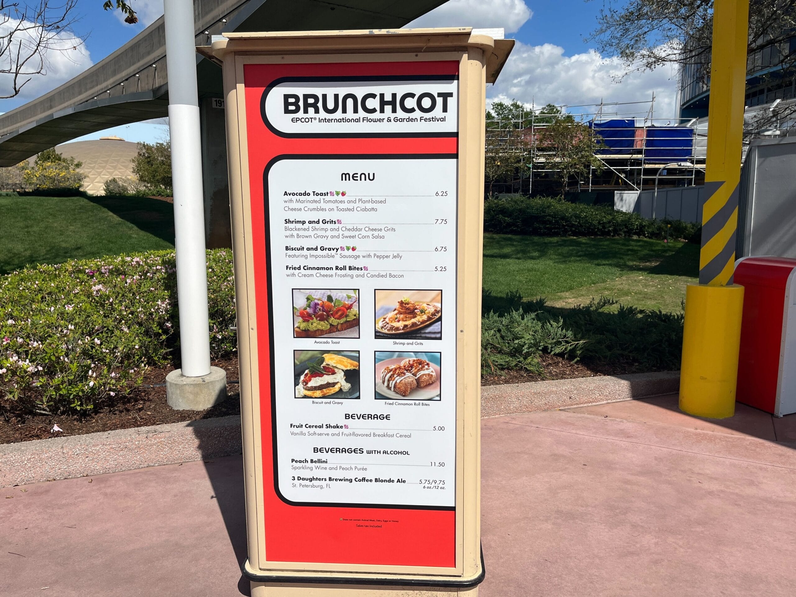 A menu board titled "BRUNCHCOT" stands proudly at the food festival, featuring delights like avocado toast, shrimp cake, and an array of beverages, each item paired with its price. The vibrant backdrop of blue sky and lush trees enhances the festive ambiance.