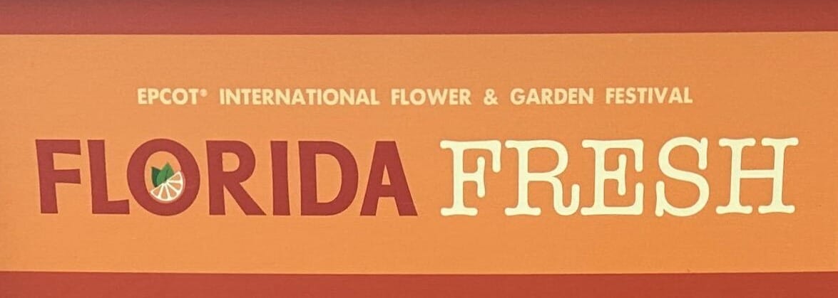 A sign reads "EPCOT International Flower & Garden Festival" elegantly showcasing the vibrant theme of Florida Fresh, adorned with a colorful citrus slice symbol.